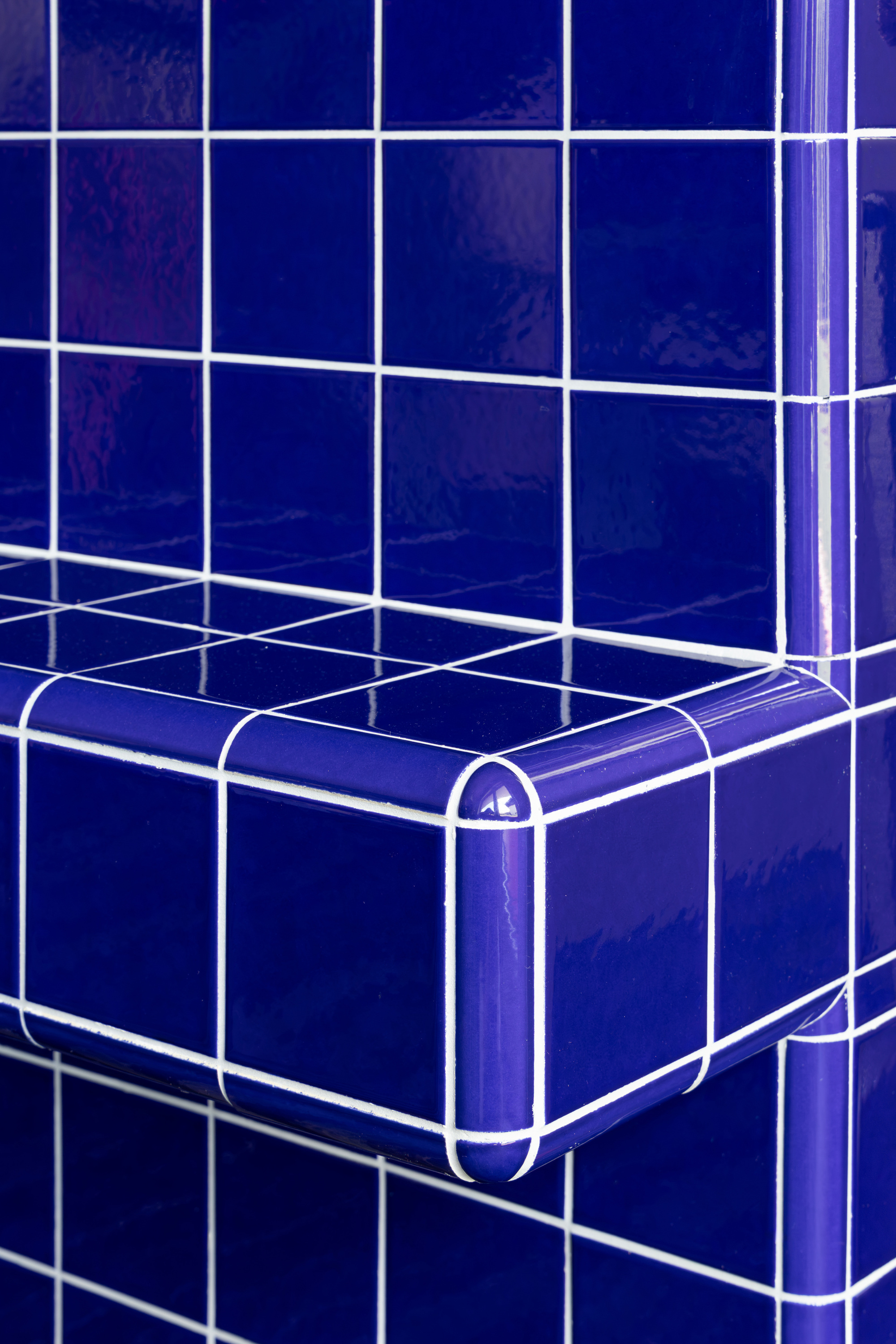 Close-up of a cobalt blue glazed tile bench corner with rounded bullnose edge trim and white grout lines