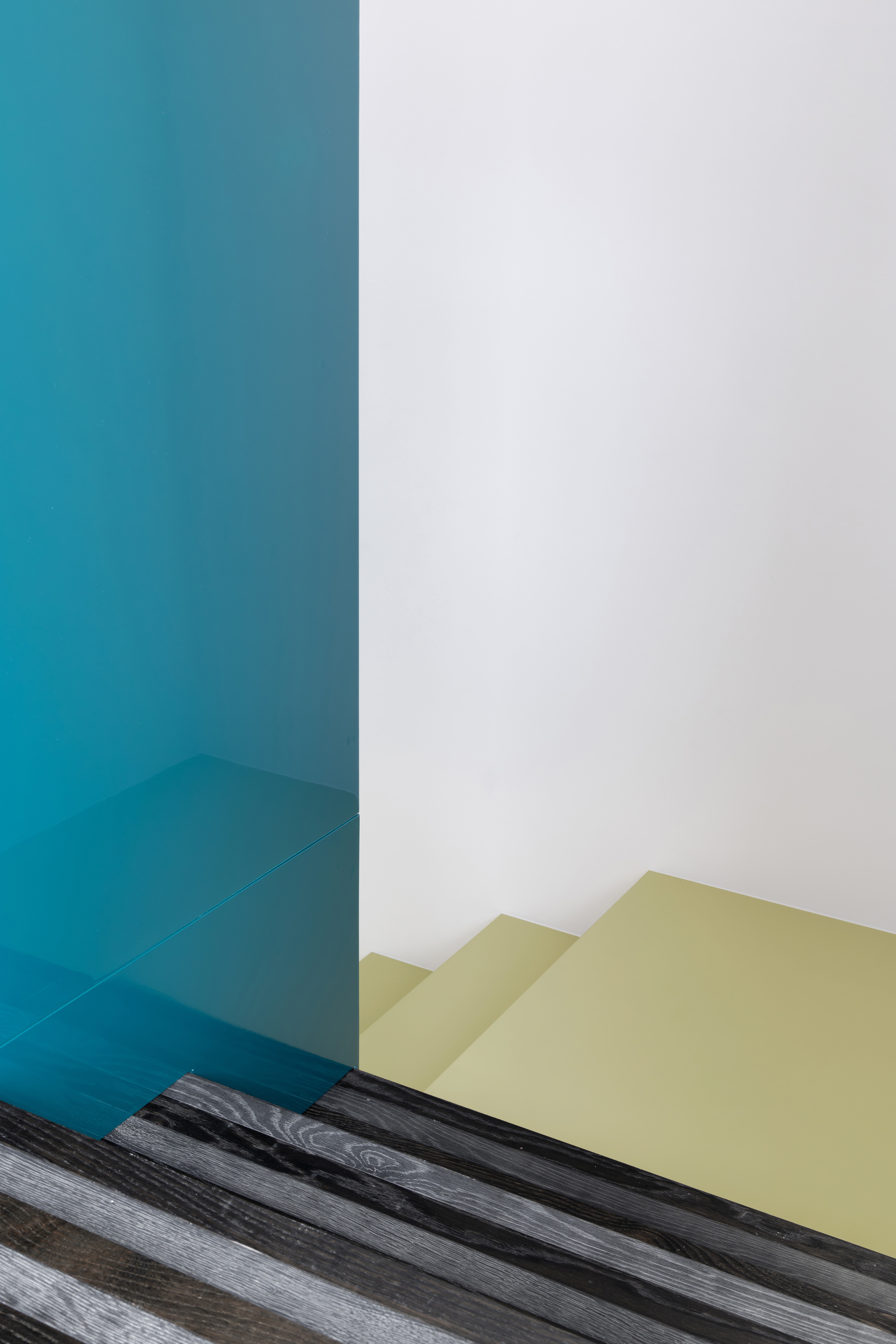 Teal translucent glass panel over a charred striped timber floor, with olive stair treads rising behind in soft light