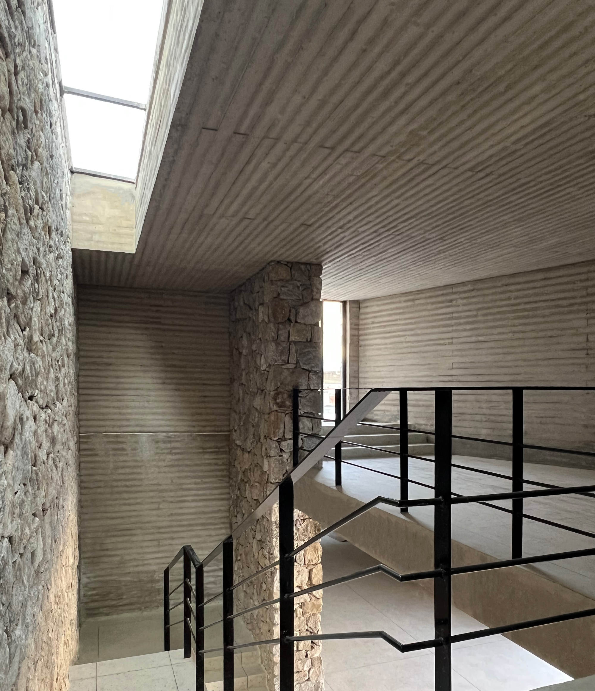 This interior photograph captures a multi-level circulation space defined by a rich contrast of tactile textures, featuring grooved, board-formed concrete and r
