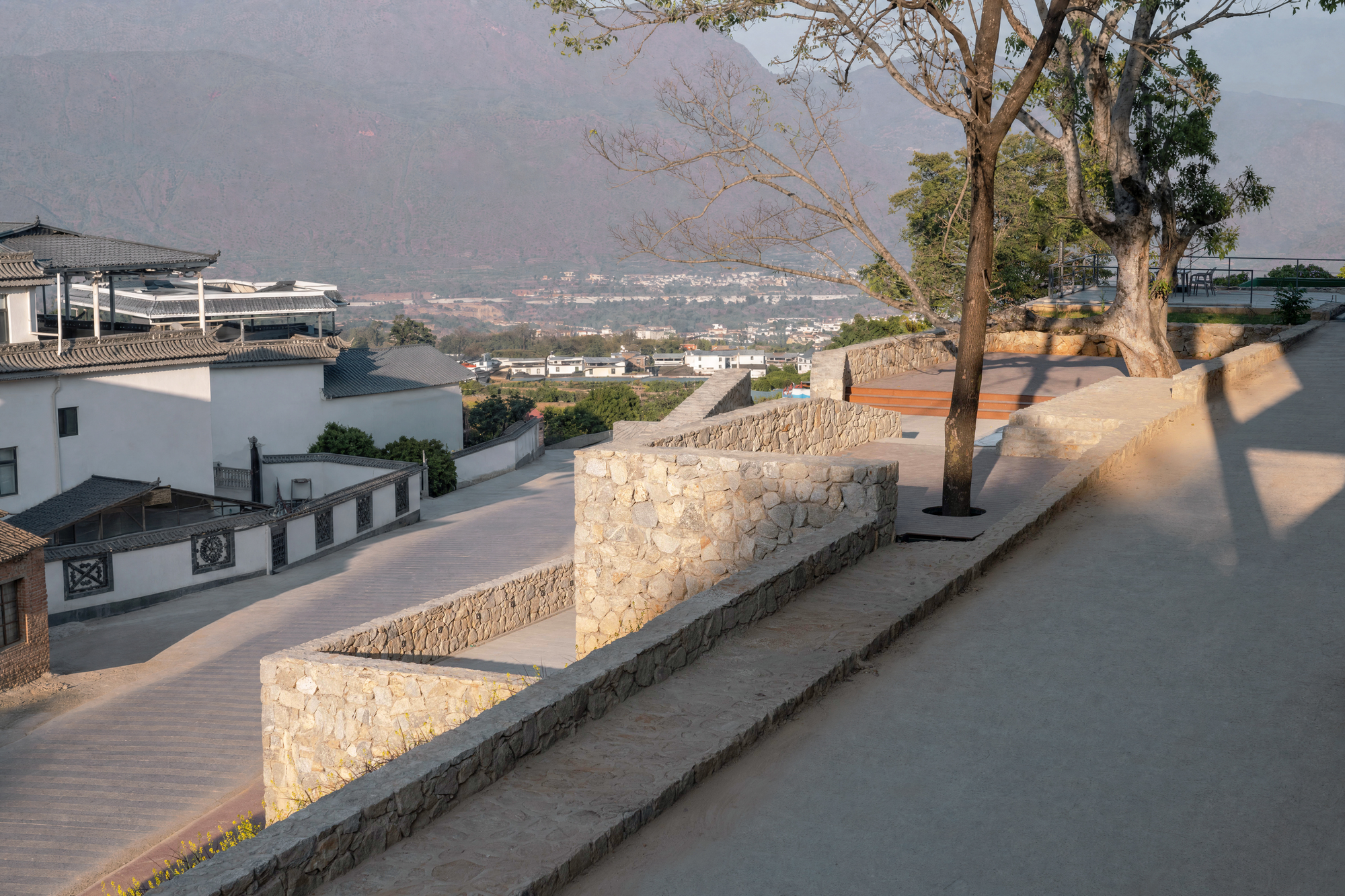 This elevated outdoor terrace features integrated stone masonry retaining walls and tiered pathways that gracefully negotiate the hillside topography. In the ba