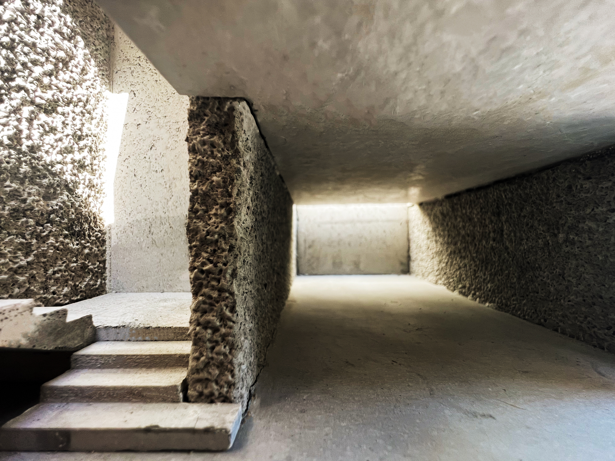 Interior of the model showing a rough aggregate wall beside a short flight of steps, with light slipping in from a side slot