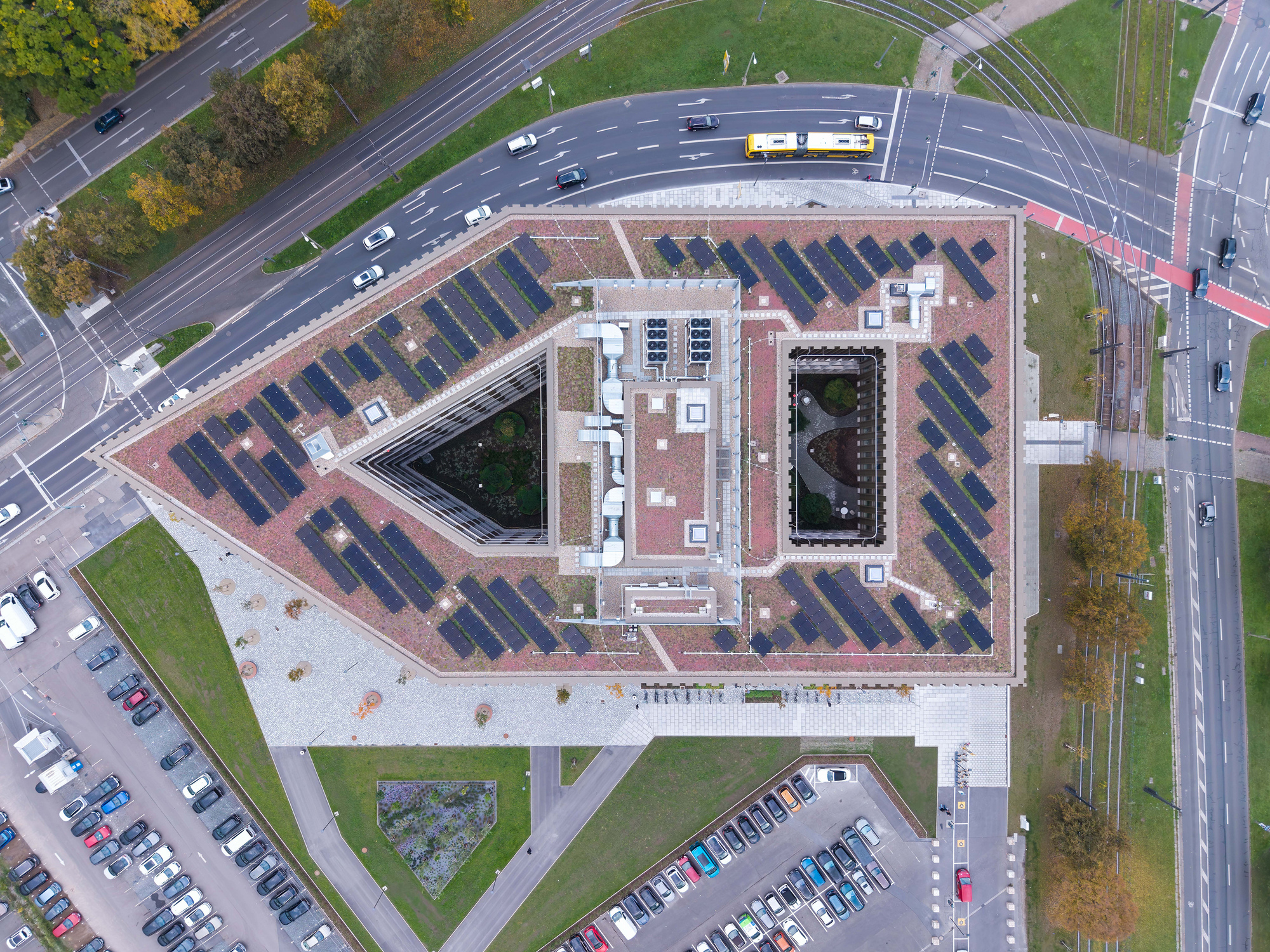 Aerial view of the green roof with solar panel rows and two courtyards, flanked by roads and a passing yellow bus
