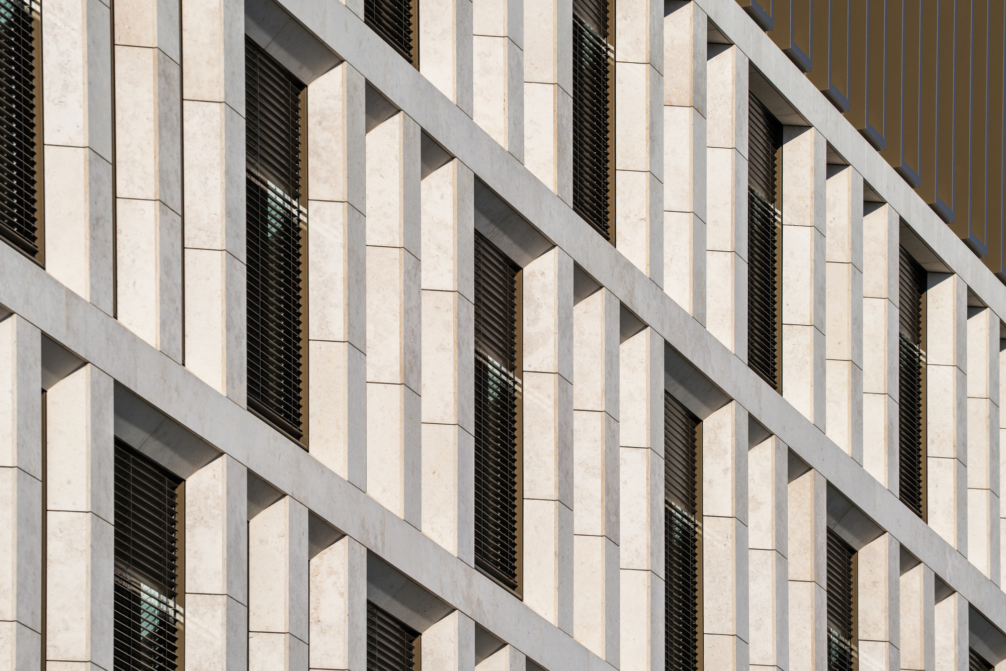 Detail of stone fins and deep window reveals with louvred blinds, lit by raking afternoon sun