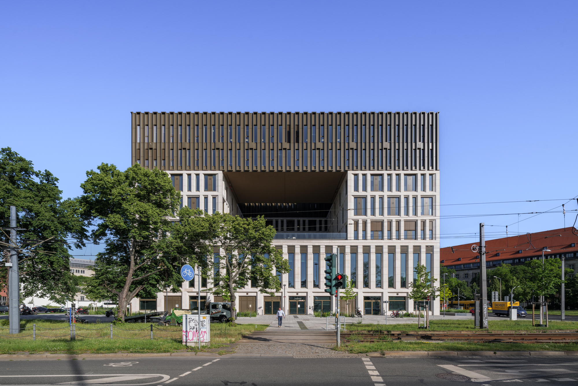 Frontal view of the stone block with a deep open recess below the finned top, a pedestrian crossing the street in front