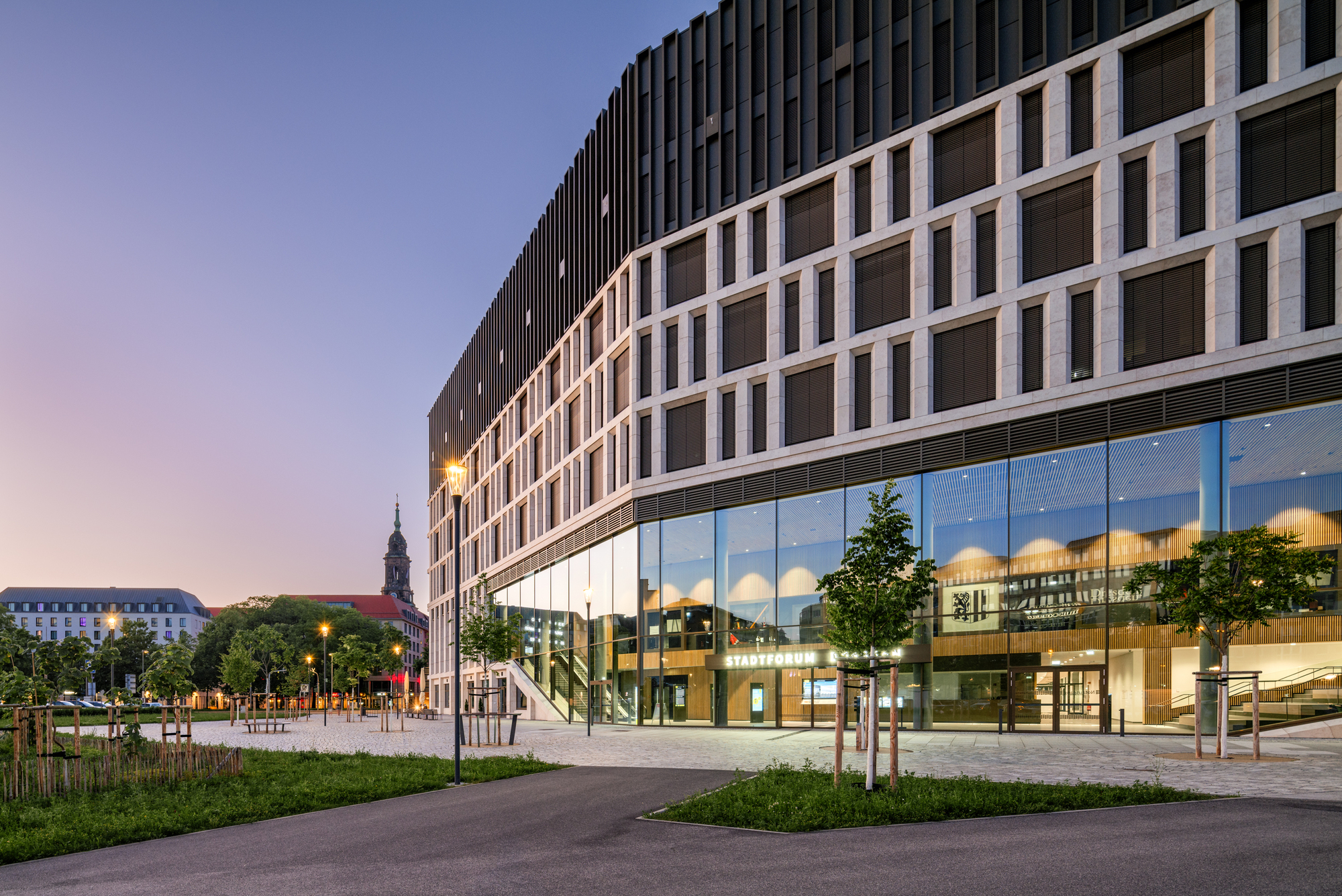Glazed ground floor and gridded stone facade with dark upper volume, seen across a lawn at dusk