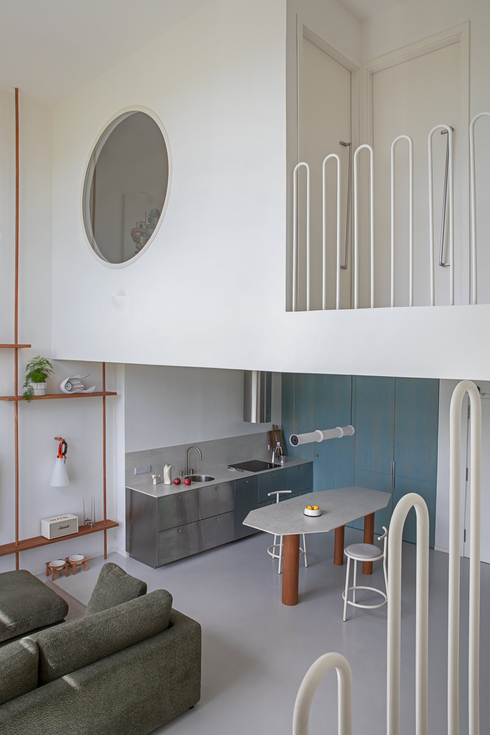 Tall interior seen from the sofa, with kitchen below, round mirror on the wall and looped white balustrade on the mezzanine