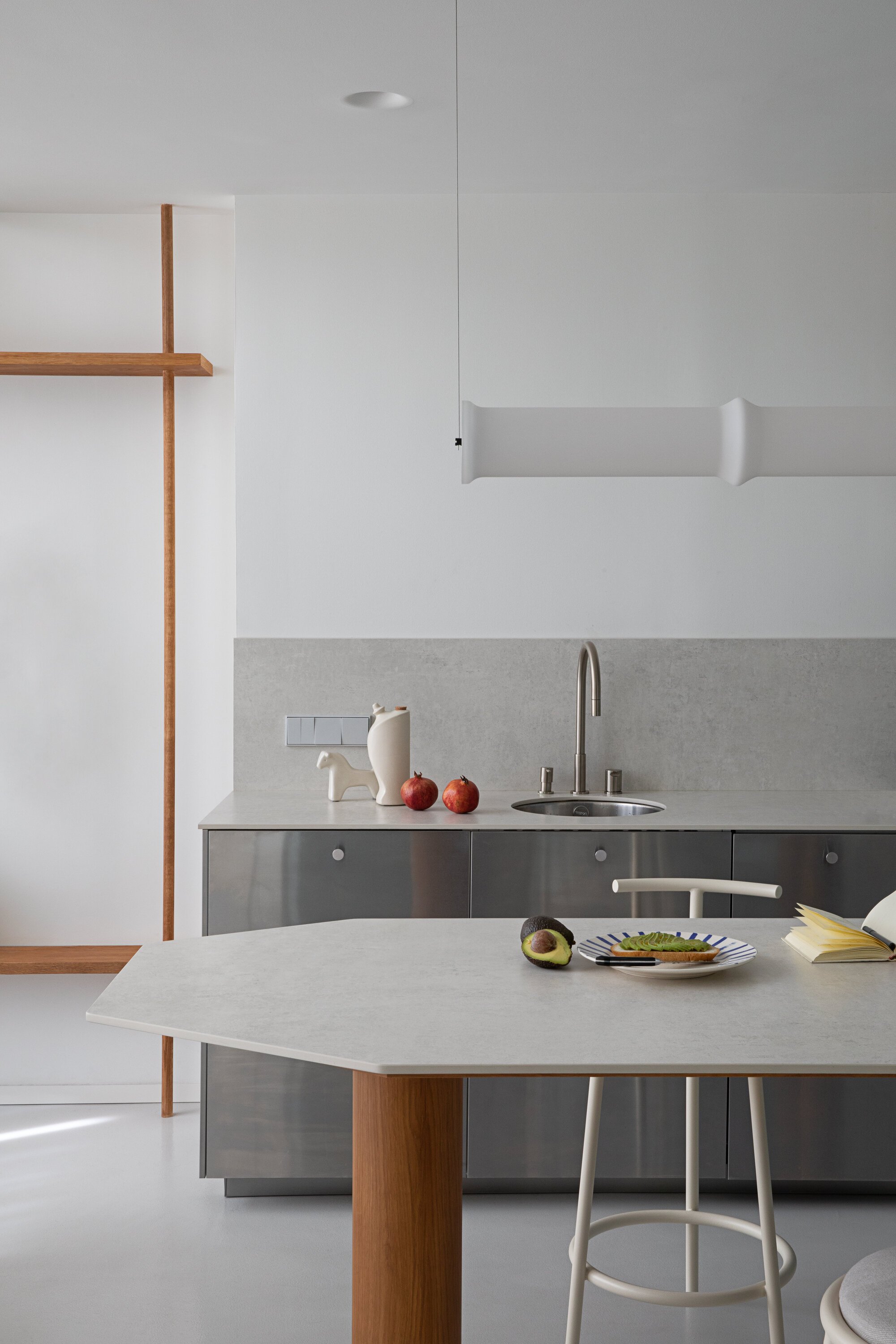 Kitchen counter with steel sink, stone backsplash and timber-framed shelf, a plate with avocado toast set on the island in soft light