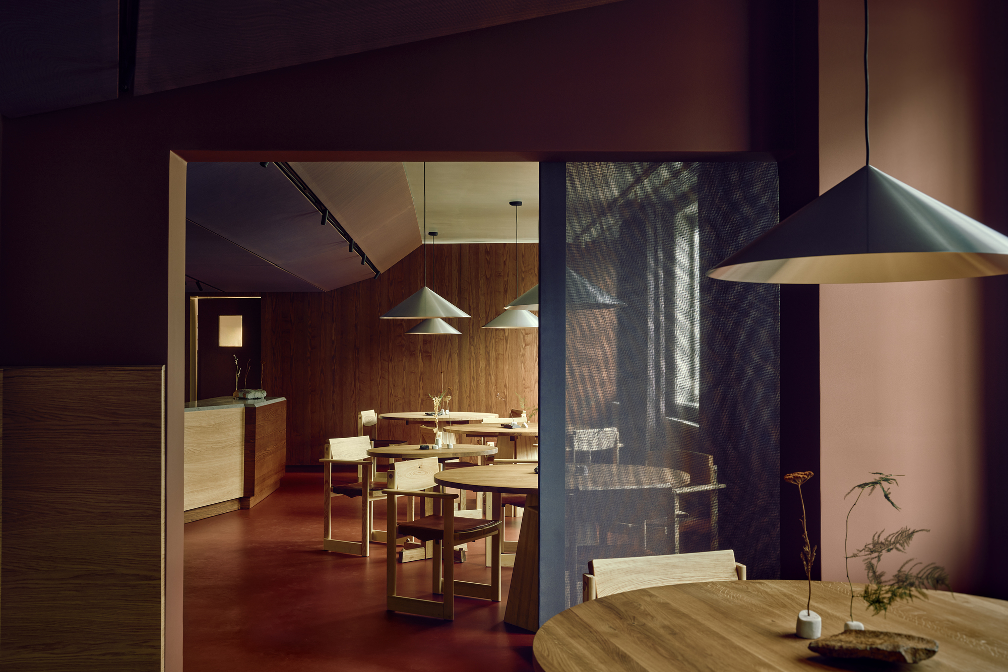 View through a doorway into the dining room, with a pink wall, mesh screen and a pendant lamp in the foreground