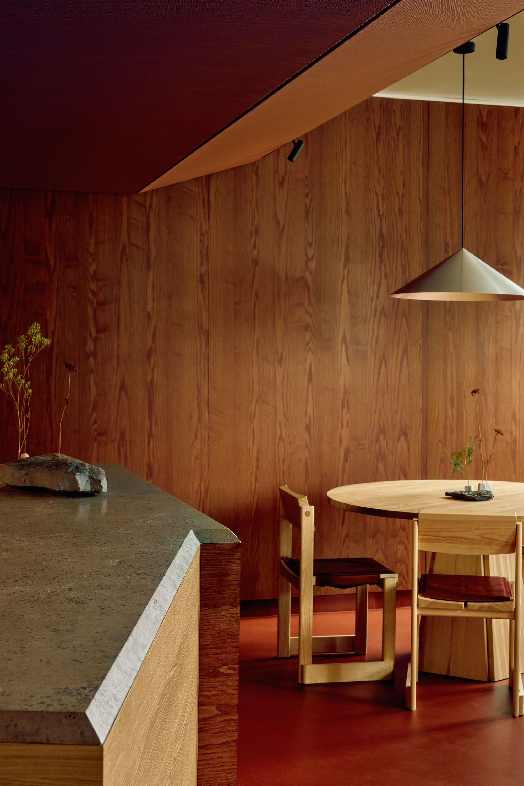 Corner of a stone-topped oak counter holding a rock and dried stems, beside oak wall paneling and a round table