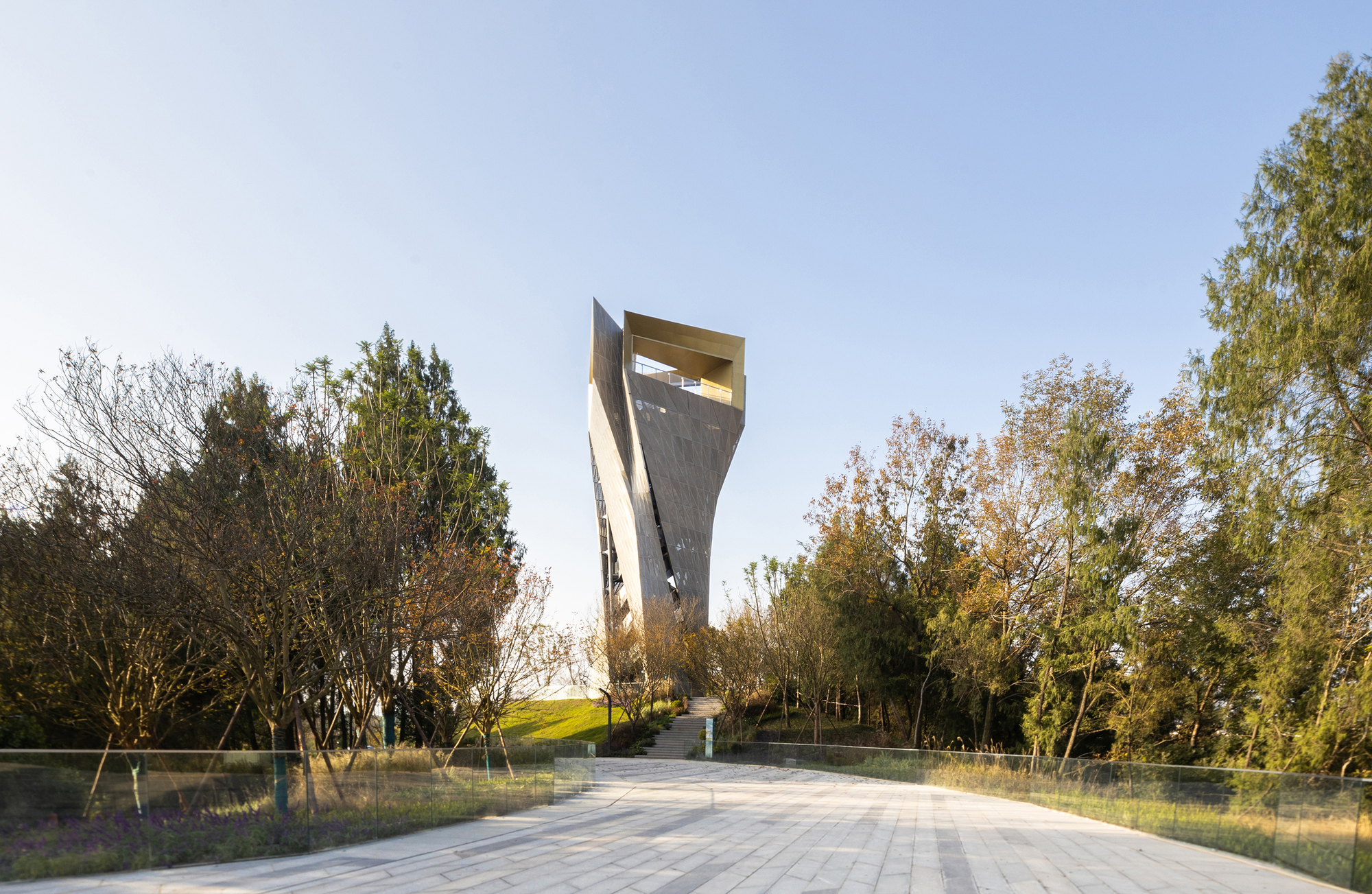 Twisting tower with a gold-lined open lookout at its top, seen along a paved path through autumn trees