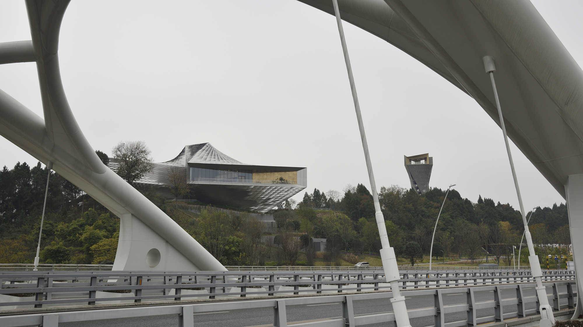 Distant view of the pavilion and lookout tower framed by white bridge arches and cable hangers on an overcast day