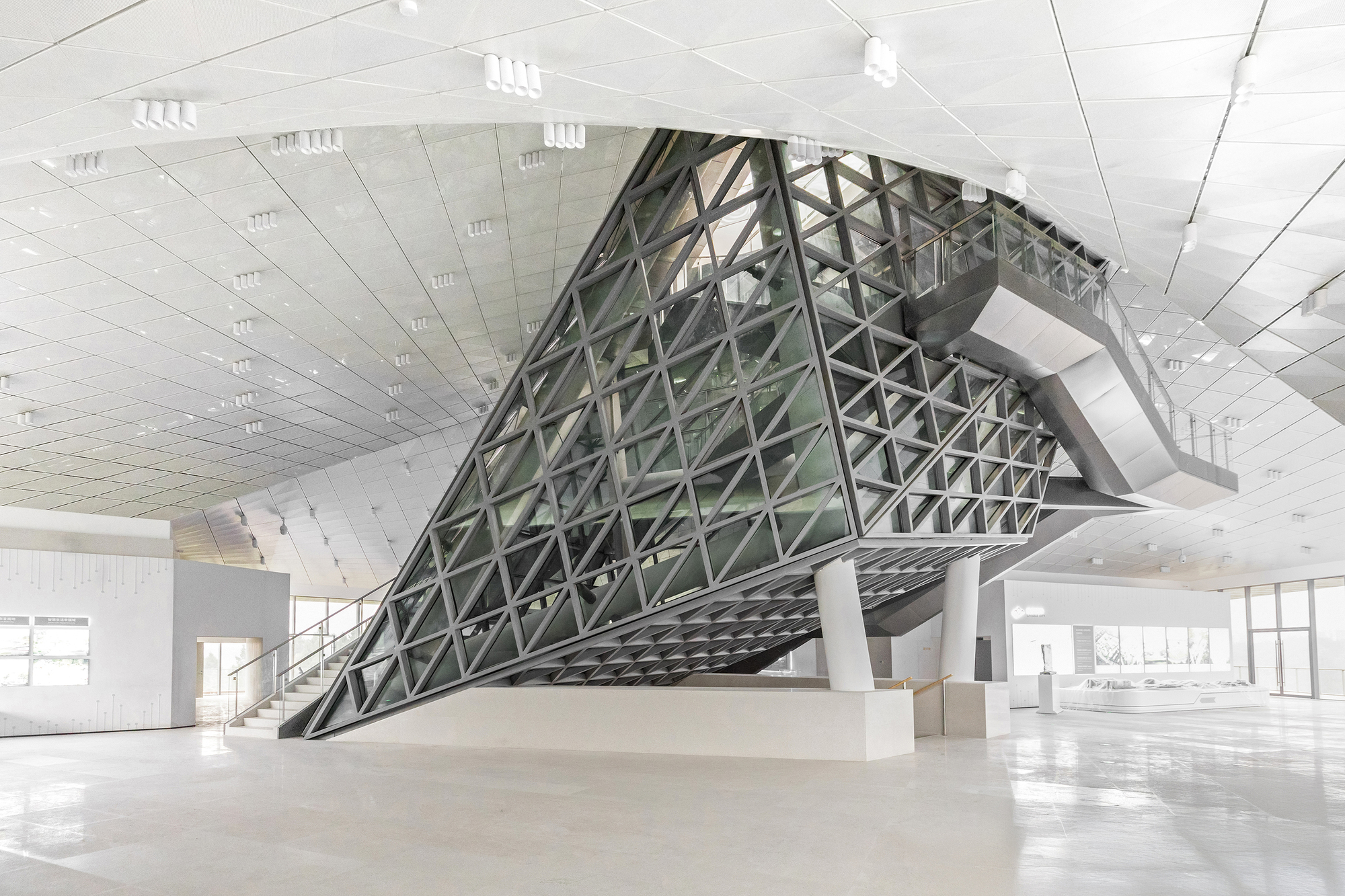 Inverted pyramid of steel lattice and glass suspended over a pale exhibition hall, with an escalator running out of its side