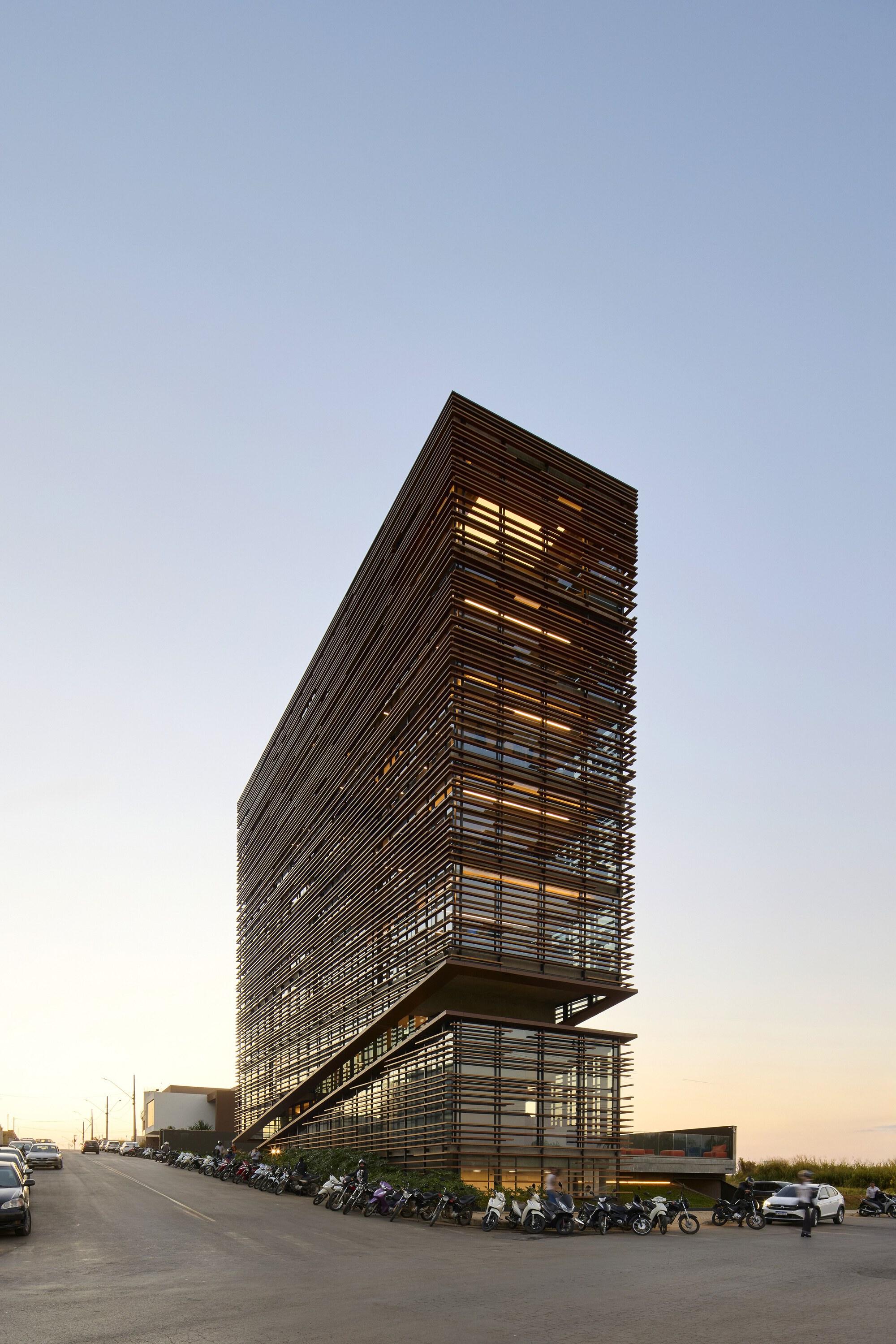Tall view of the louvered tower with lit interior floors and a row of parked motorcycles along the street at dusk