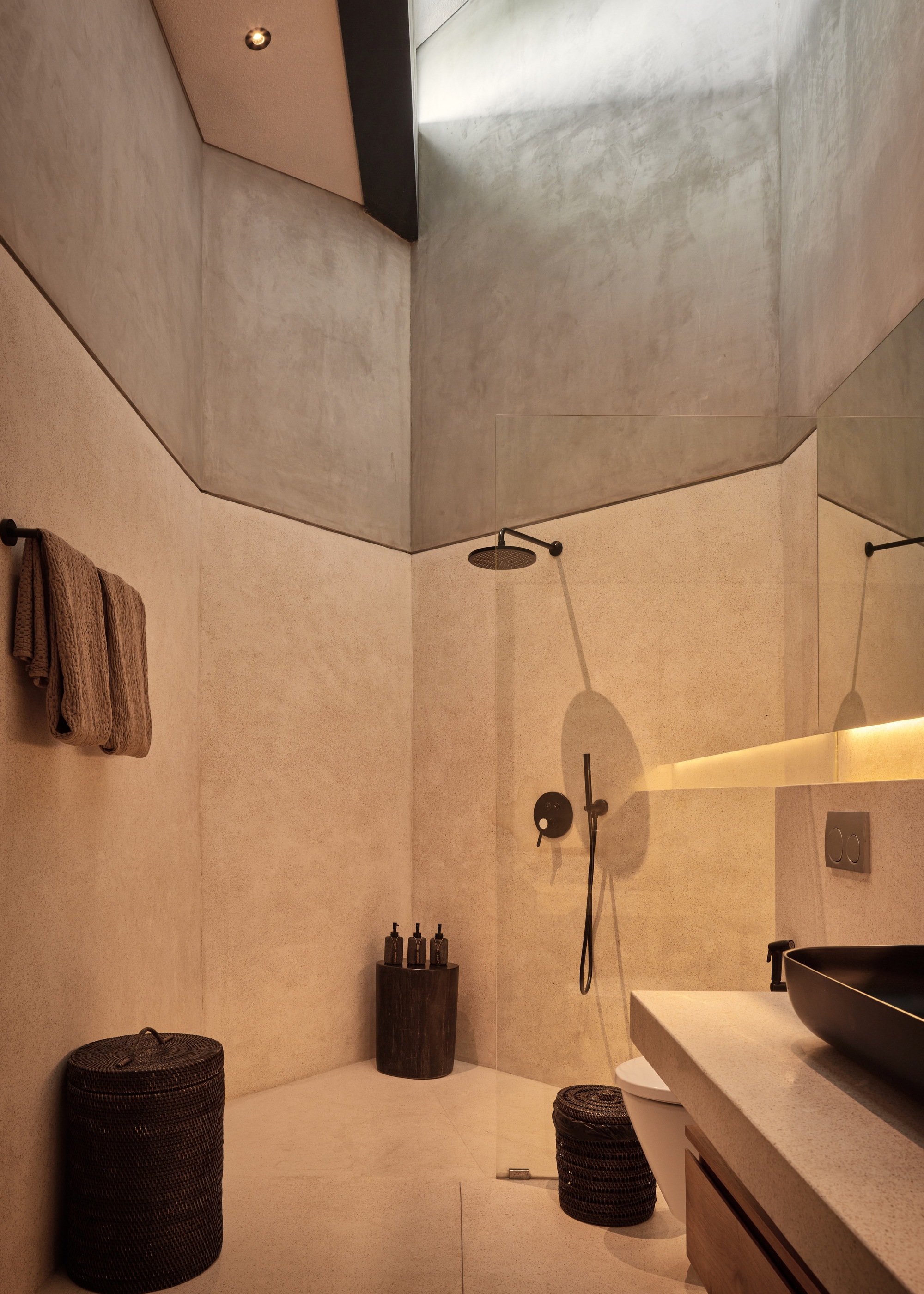 Bathroom with an open shower, black fixtures and a basin, daylight falling down tall angled plaster walls above