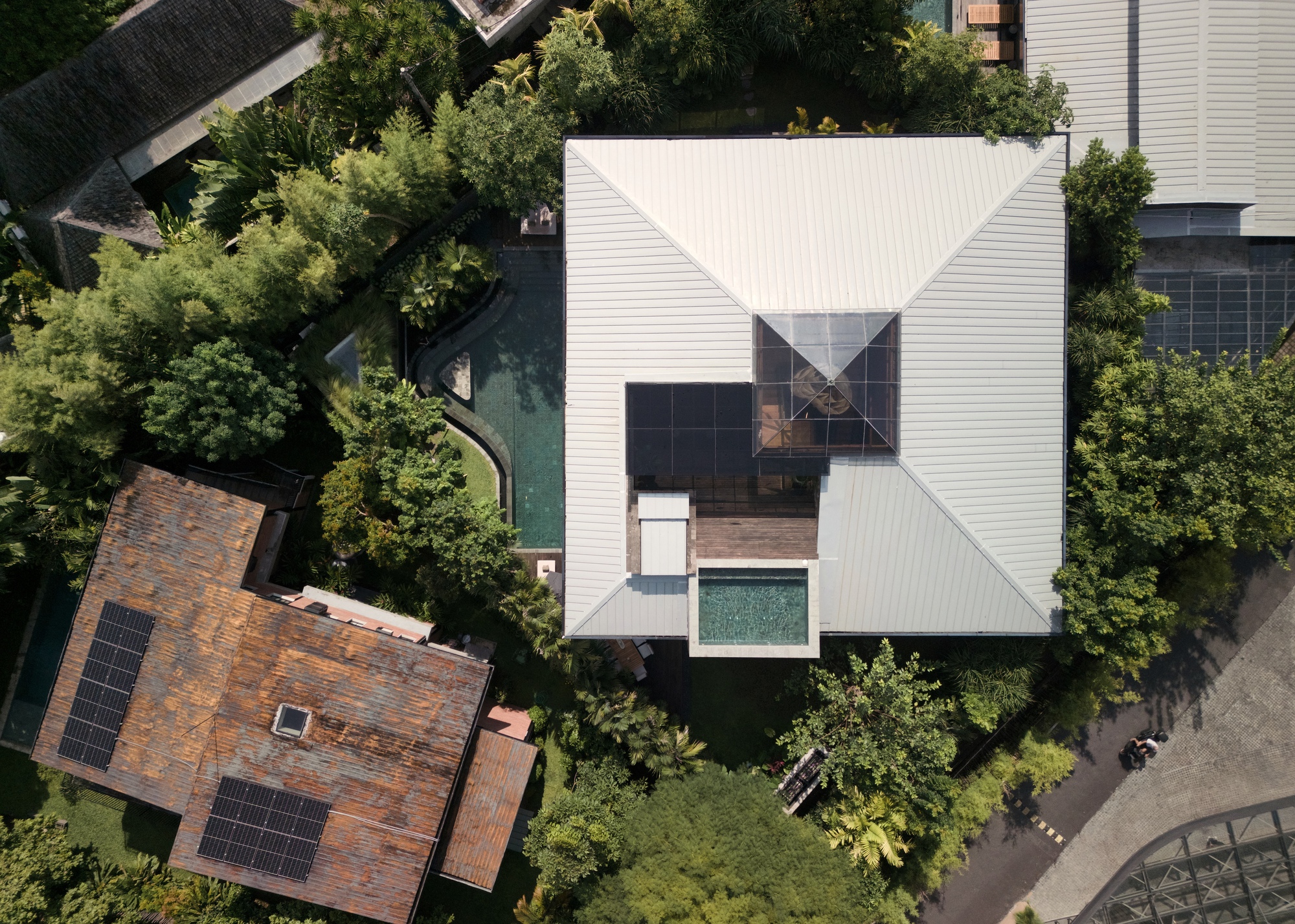 Aerial view of the pyramidal white metal roof with a glazed skylight and small plunge pool among tropical trees