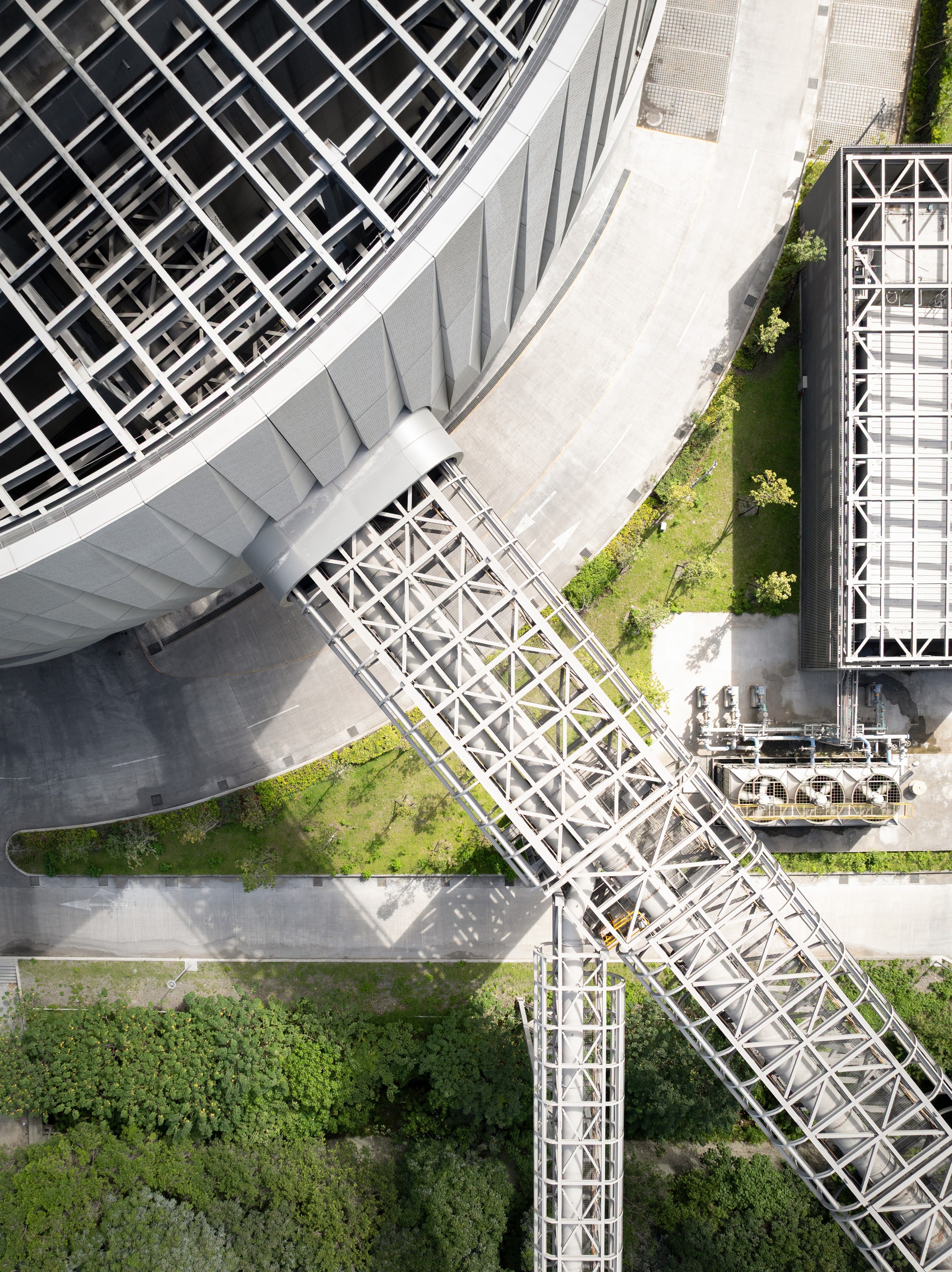 Top-down drone view of the diagonal truss bridge crossing a road and lawn beside the circular roof