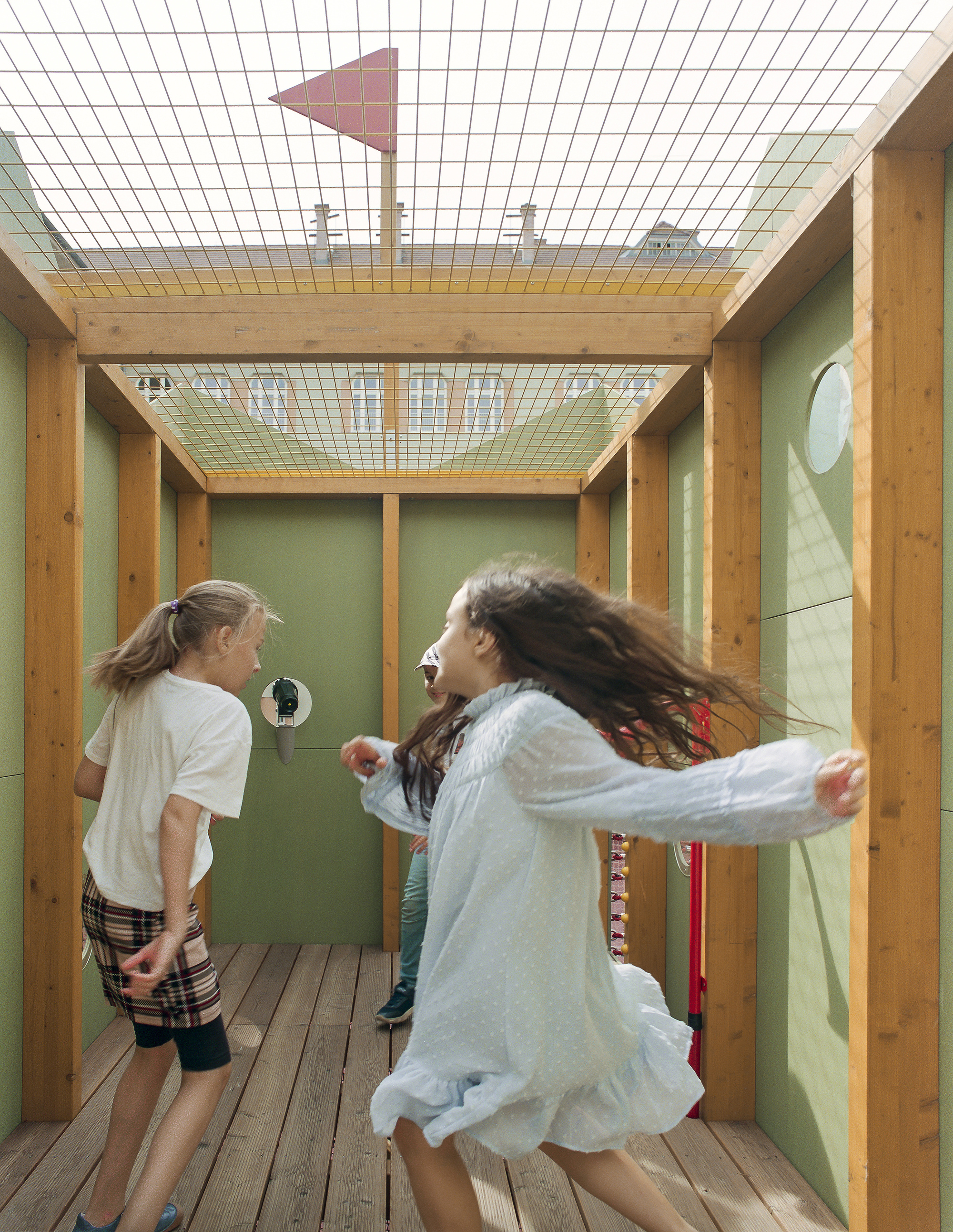 Two girls spinning on a plank deck inside a timber frame with green panels and a mesh roof overhead