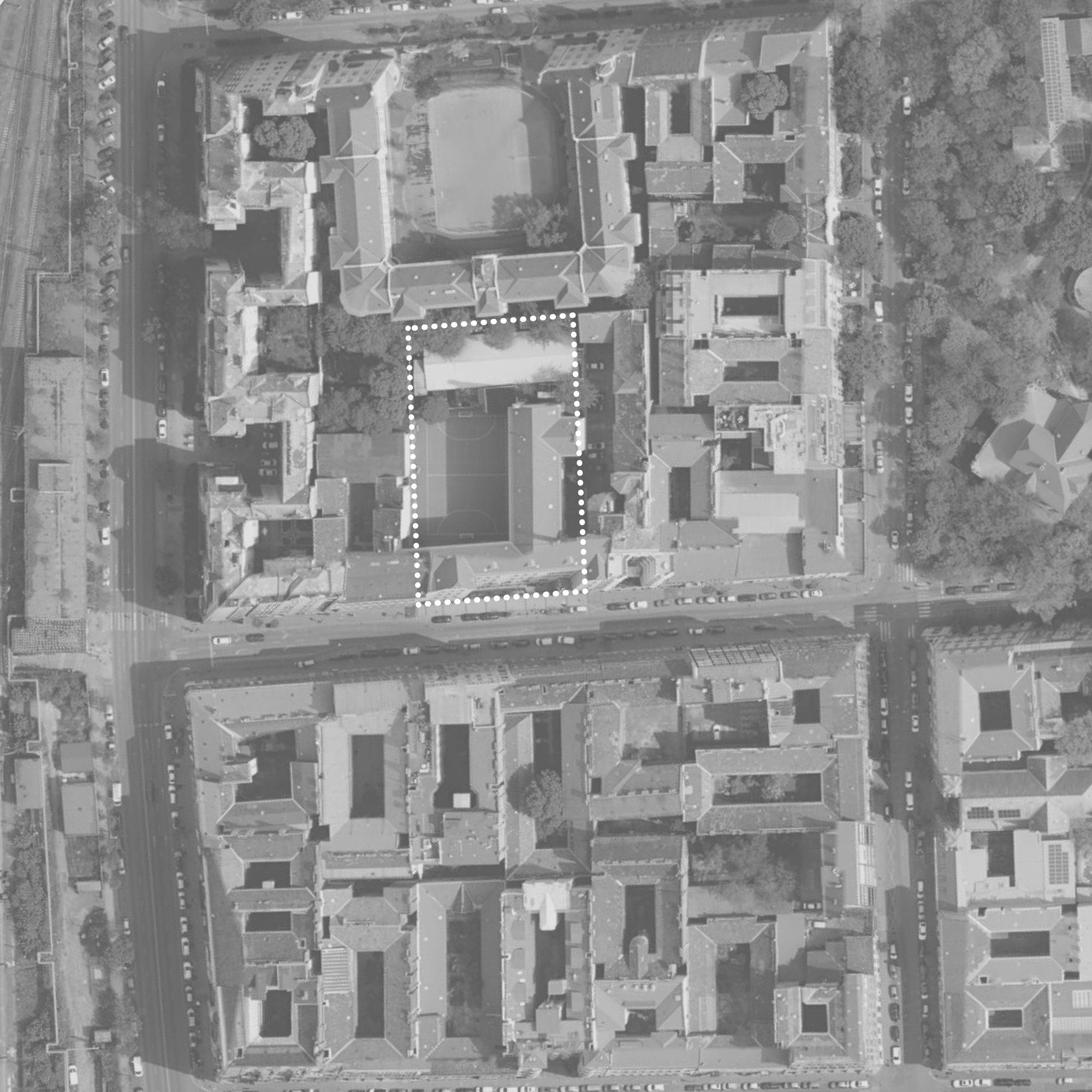 Grayscale aerial photograph of a dense urban block with a dotted line outlining the school courtyard site