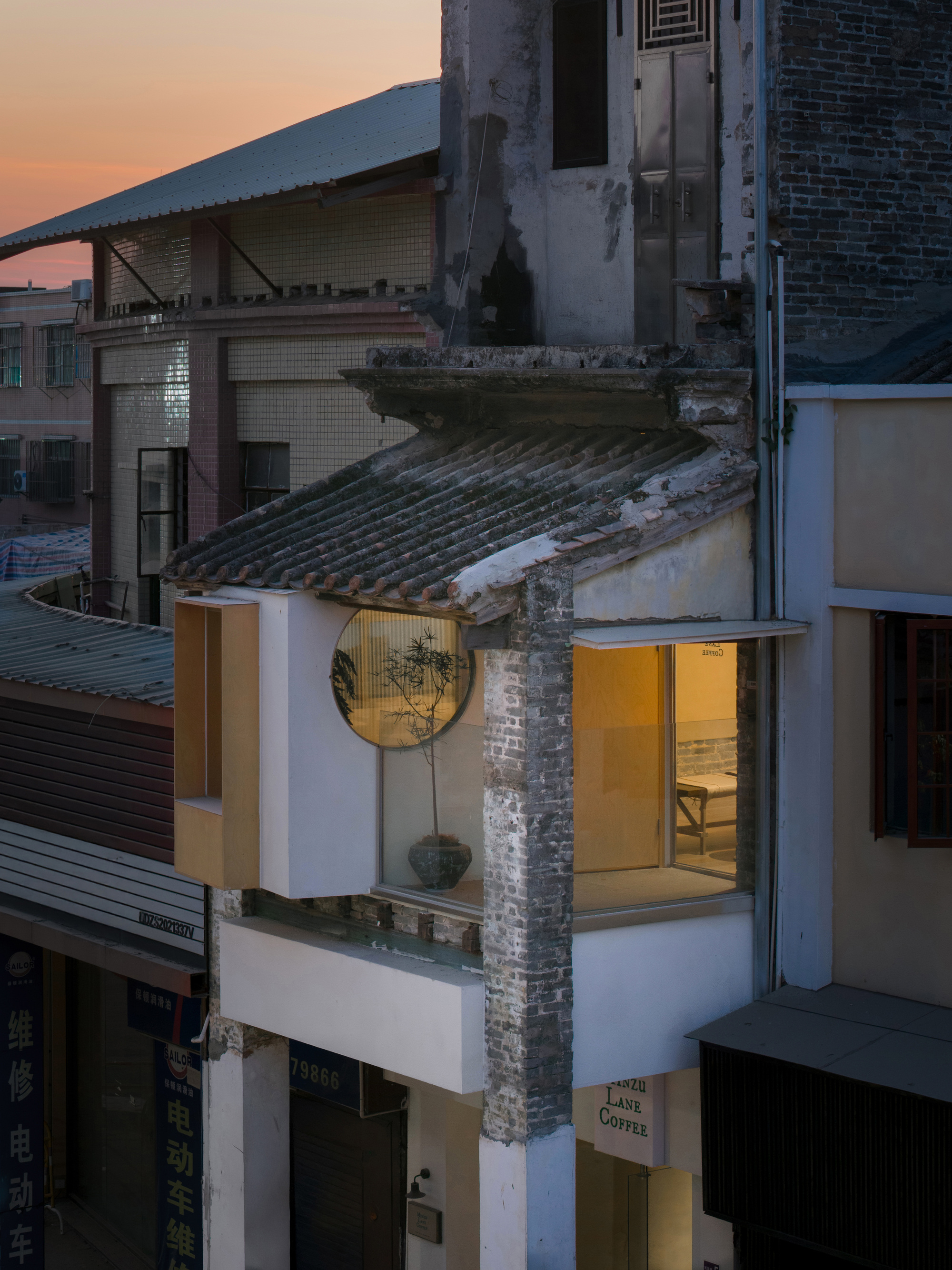 Corner view of the tiled eave and round window glowing warm above the street under an orange evening sky