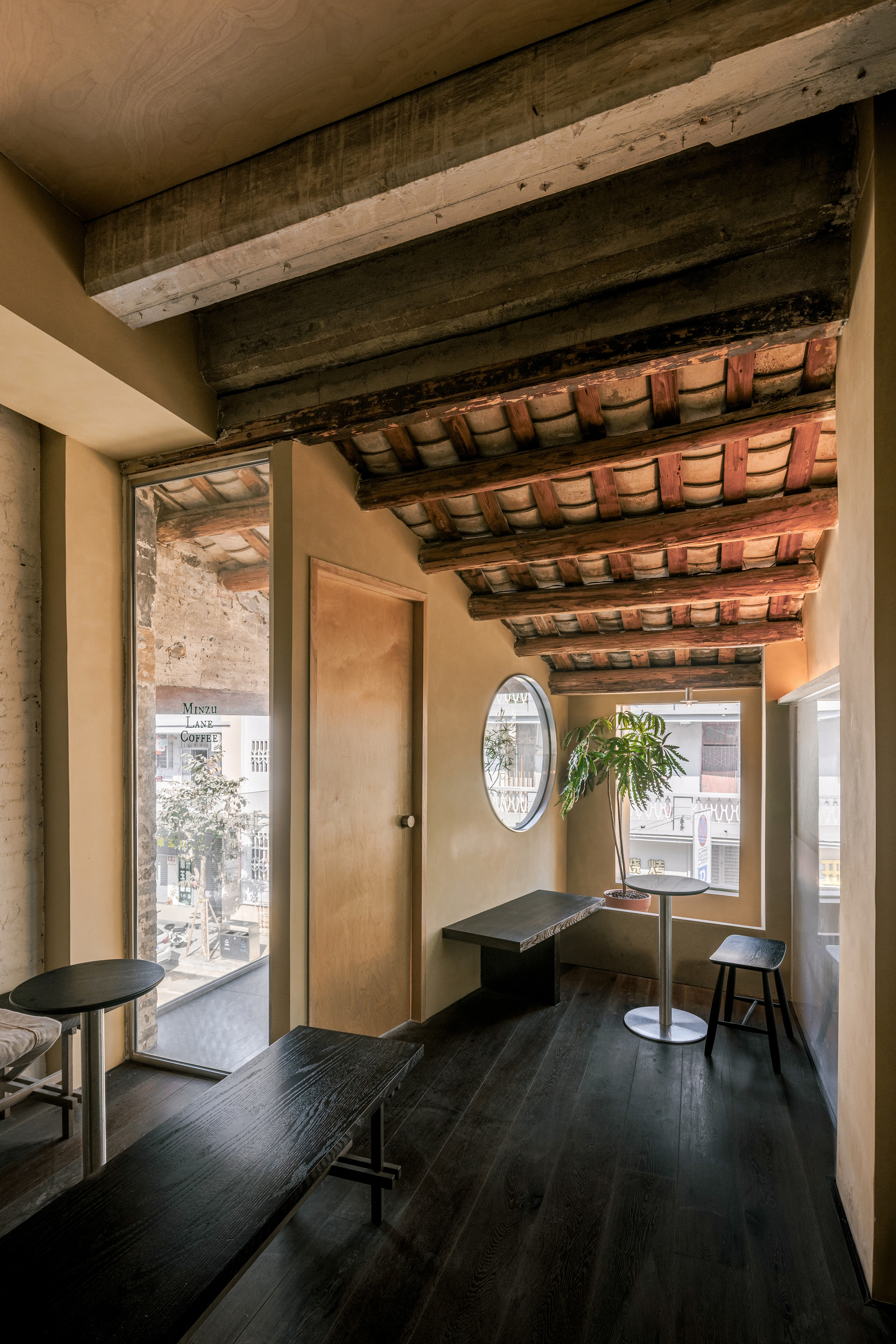 Upper-floor seating nook with exposed clay tile ceiling, dark plank floor, a round window and a potted plant in daylight