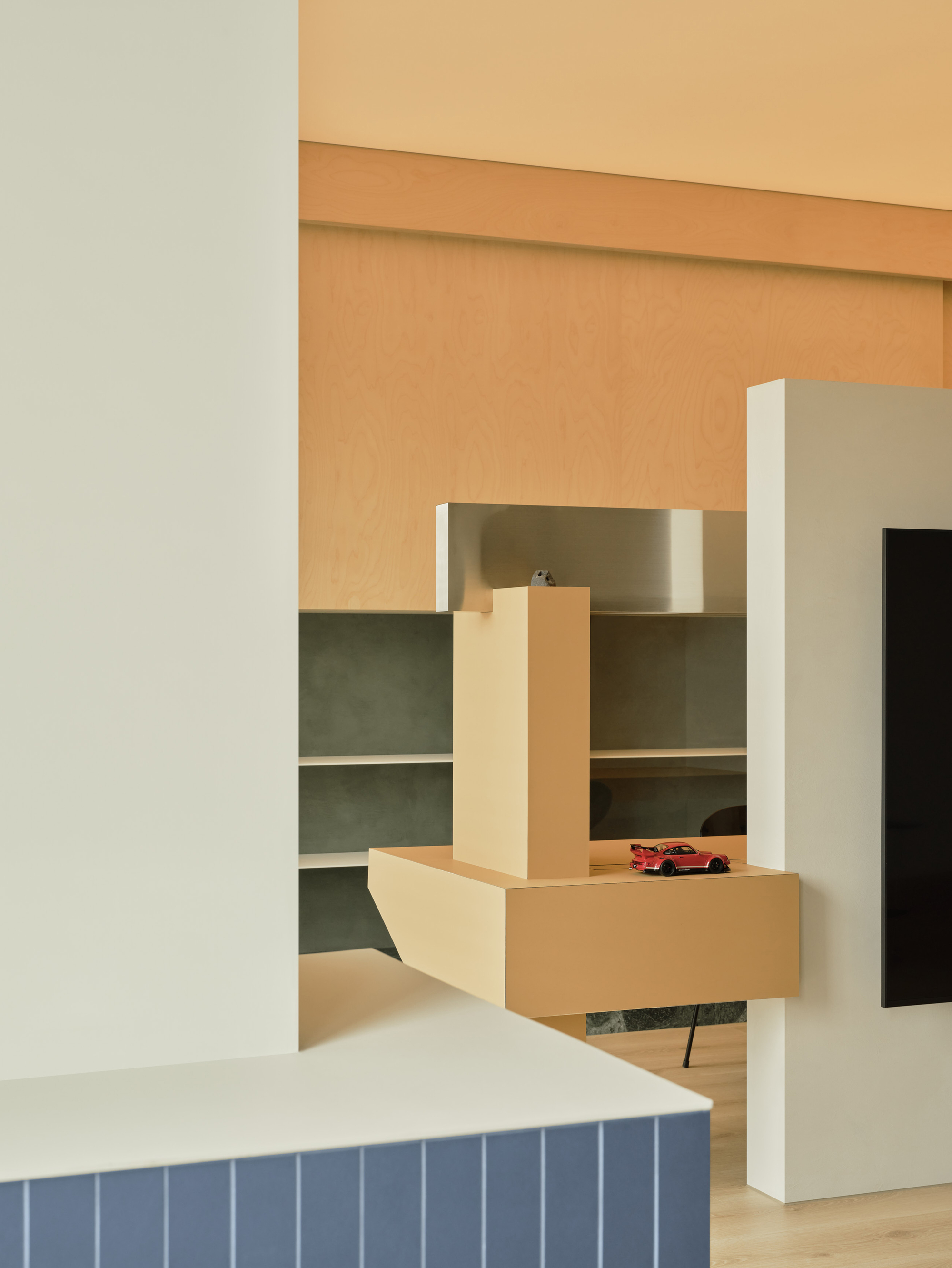 Layered cabinetry in ochre and white with a small red toy car on a cantilevered shelf in warm light