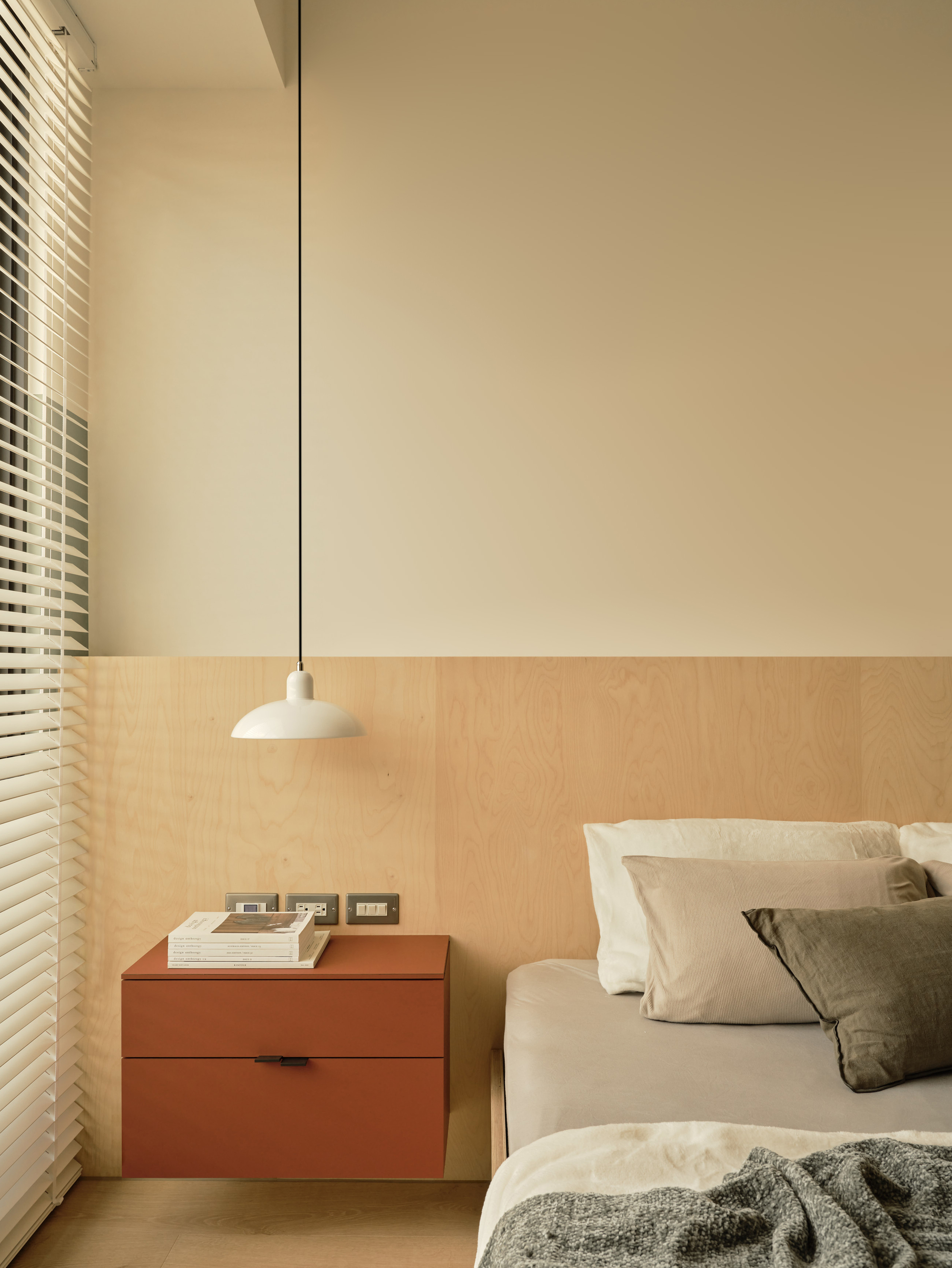 Rust-colored floating nightstand beneath a white pendant lamp, with a birch plywood wall panel and window blinds at the bedside