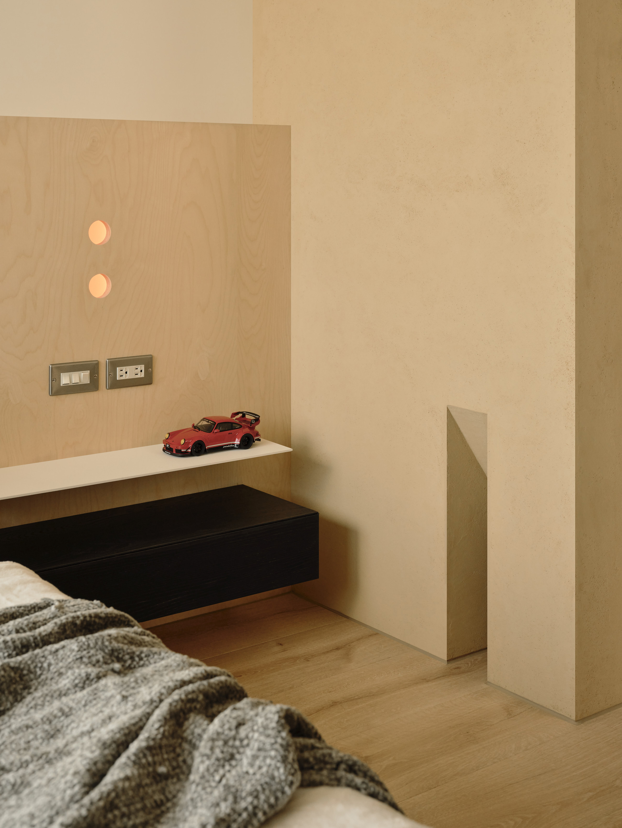 Birch headboard panel with two glowing round cutouts above a shelf holding a small red toy car, beside a plaster wall niche