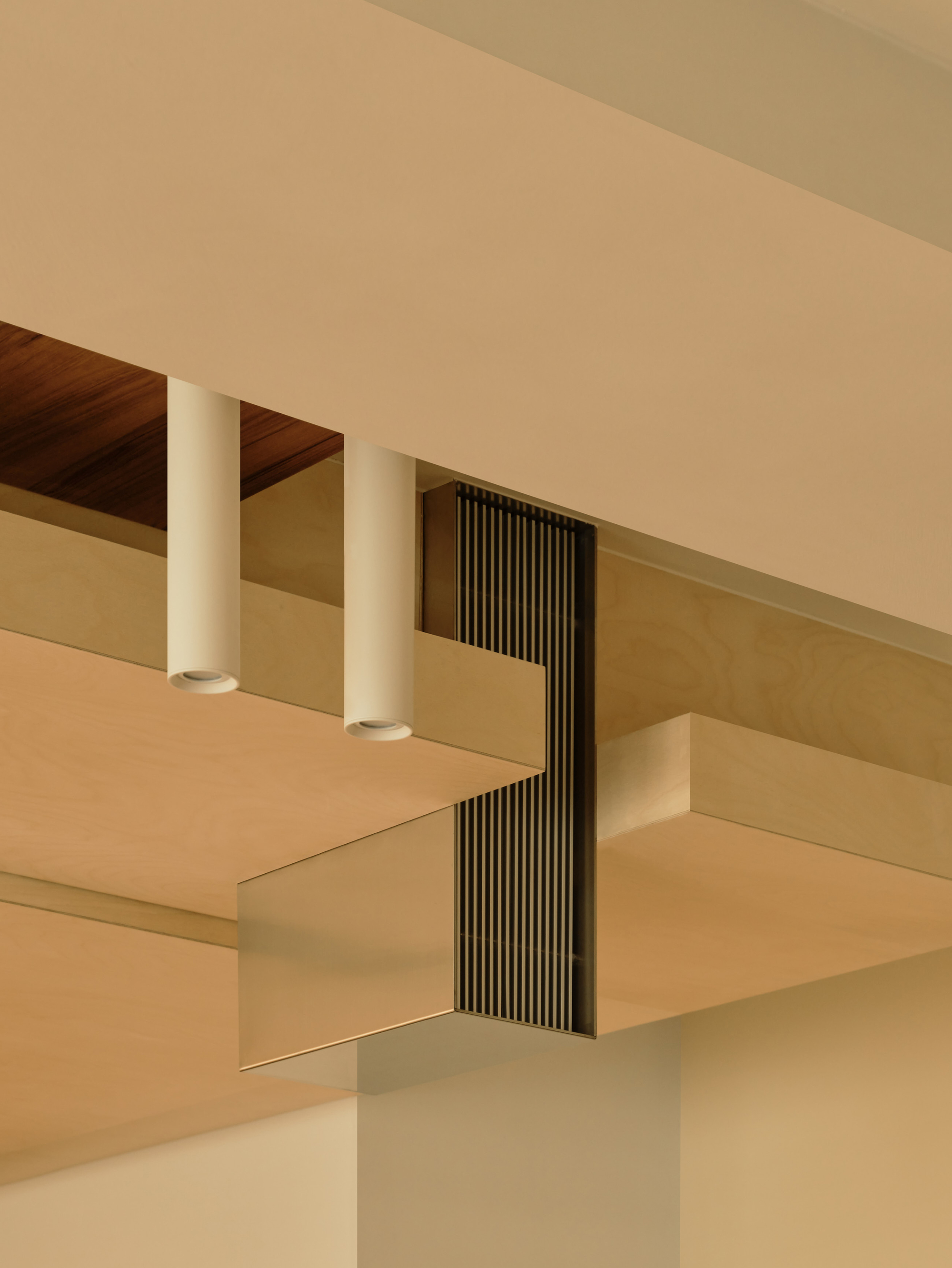 Birch plywood ceiling soffits with two white cylindrical downlights and a slatted metal vent grille, lit by warm afternoon light
