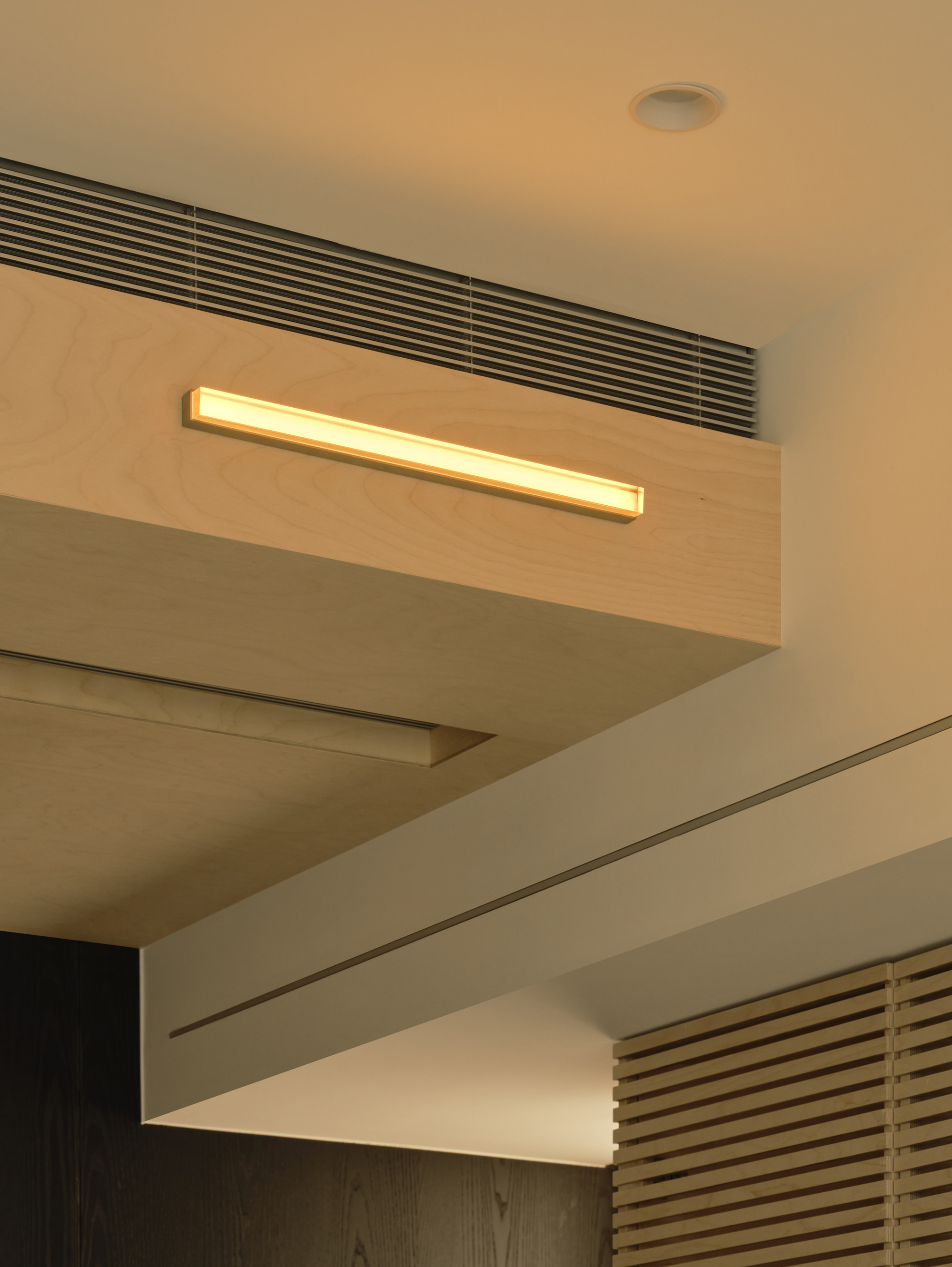 Corner of a plywood ceiling box with a linear glowing light fixture above a dark wood panel and timber slats