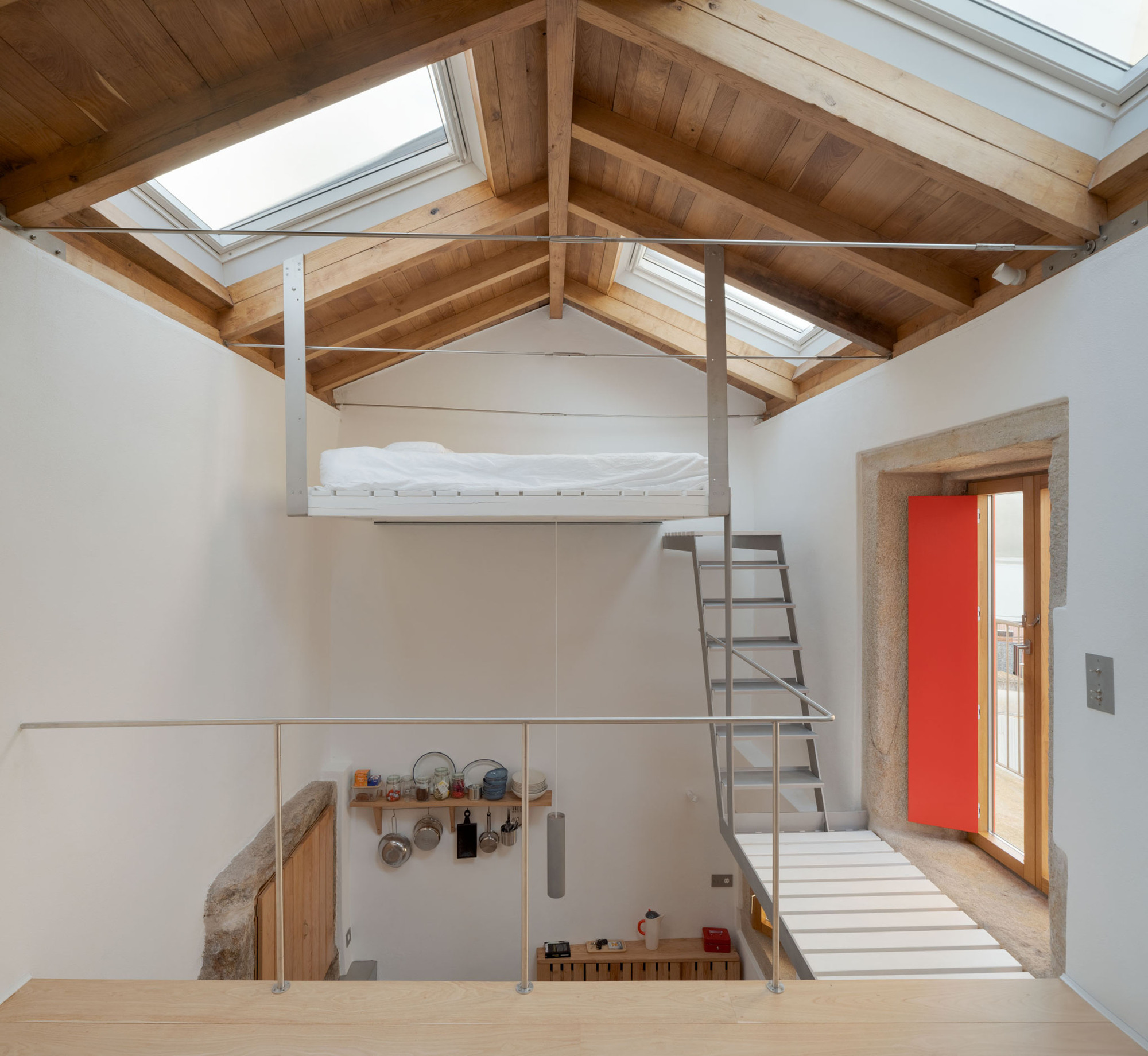 Interior with a suspended white bed platform, steel stair and skylights between exposed timber rafters in daylight
