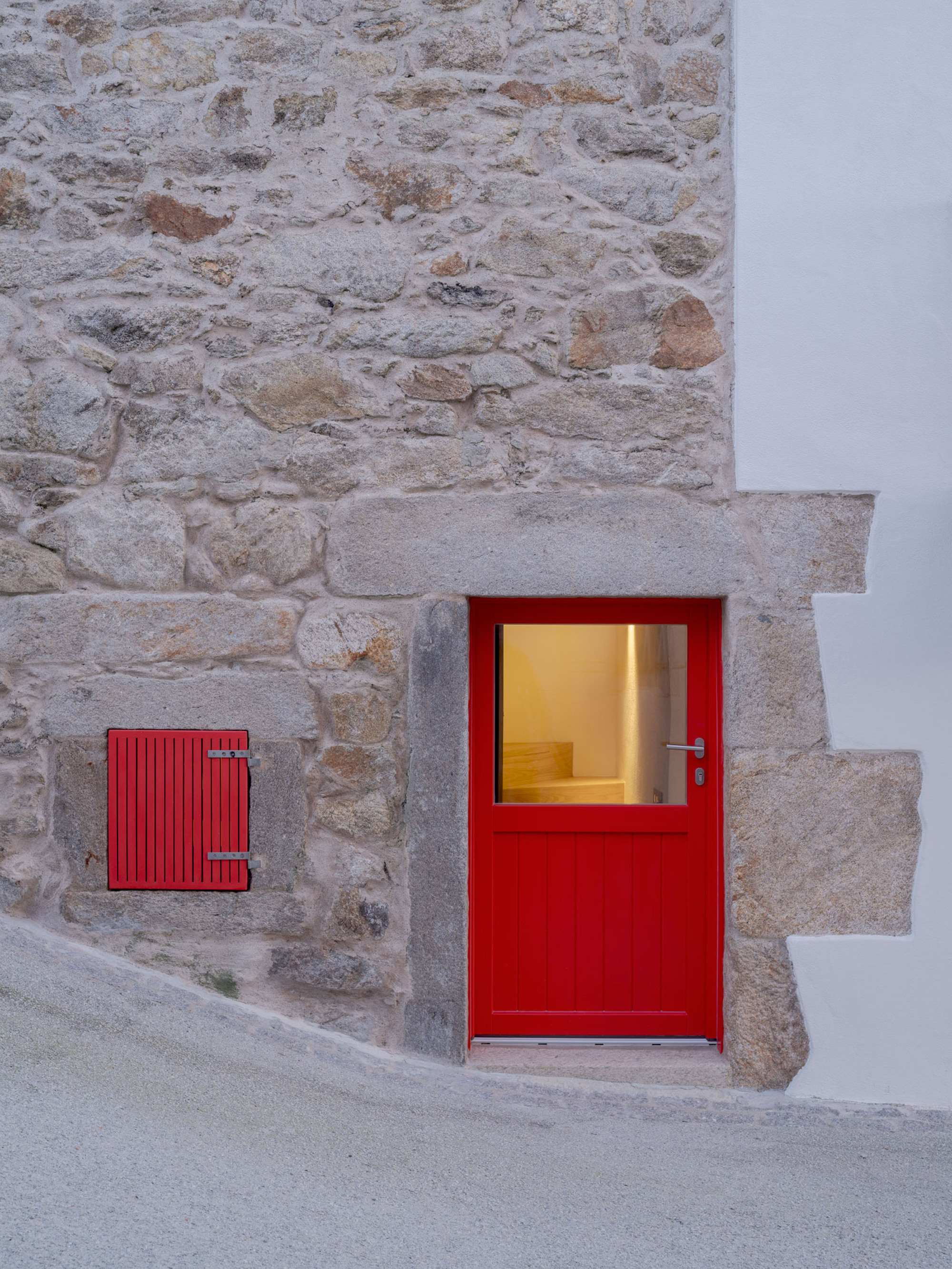 Close view of a red half-glazed door and small shutter set in rubble stone wall with granite lintel