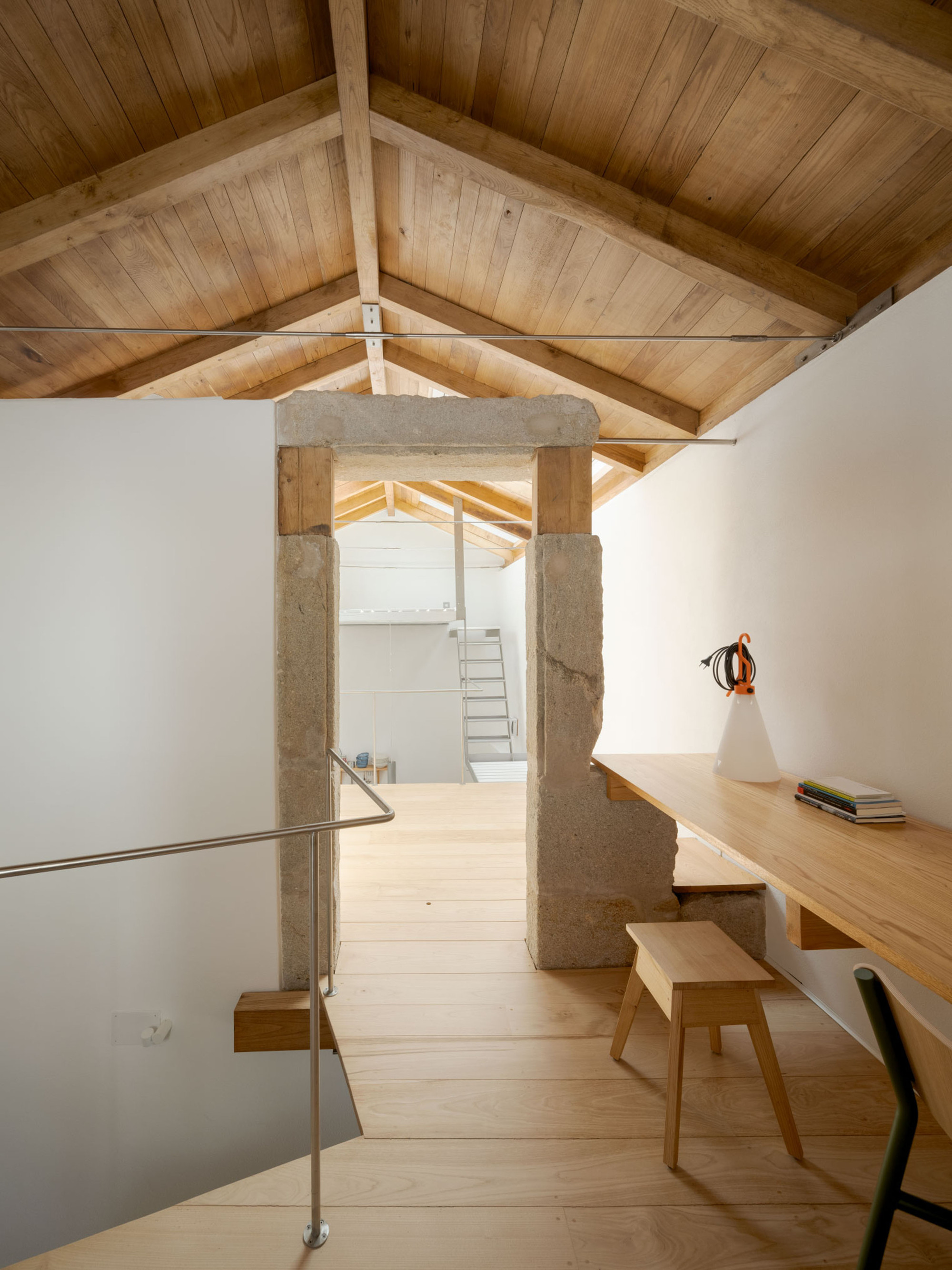 Attic loft with exposed timber rafters, a granite doorway frame, a built-in oak desk and a wooden stool in soft daylight