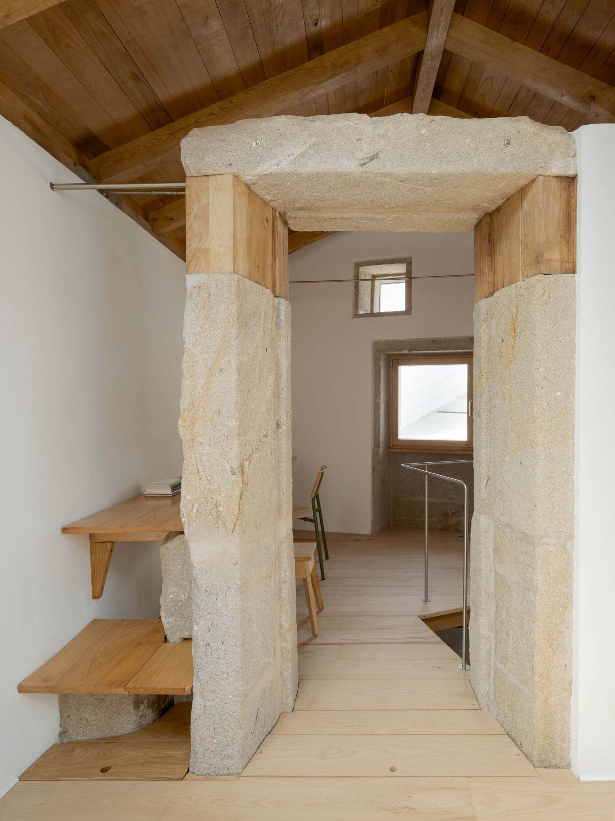 Stone and timber portal framing a doorway, with a pale plank floor and small windows glowing in the far wall