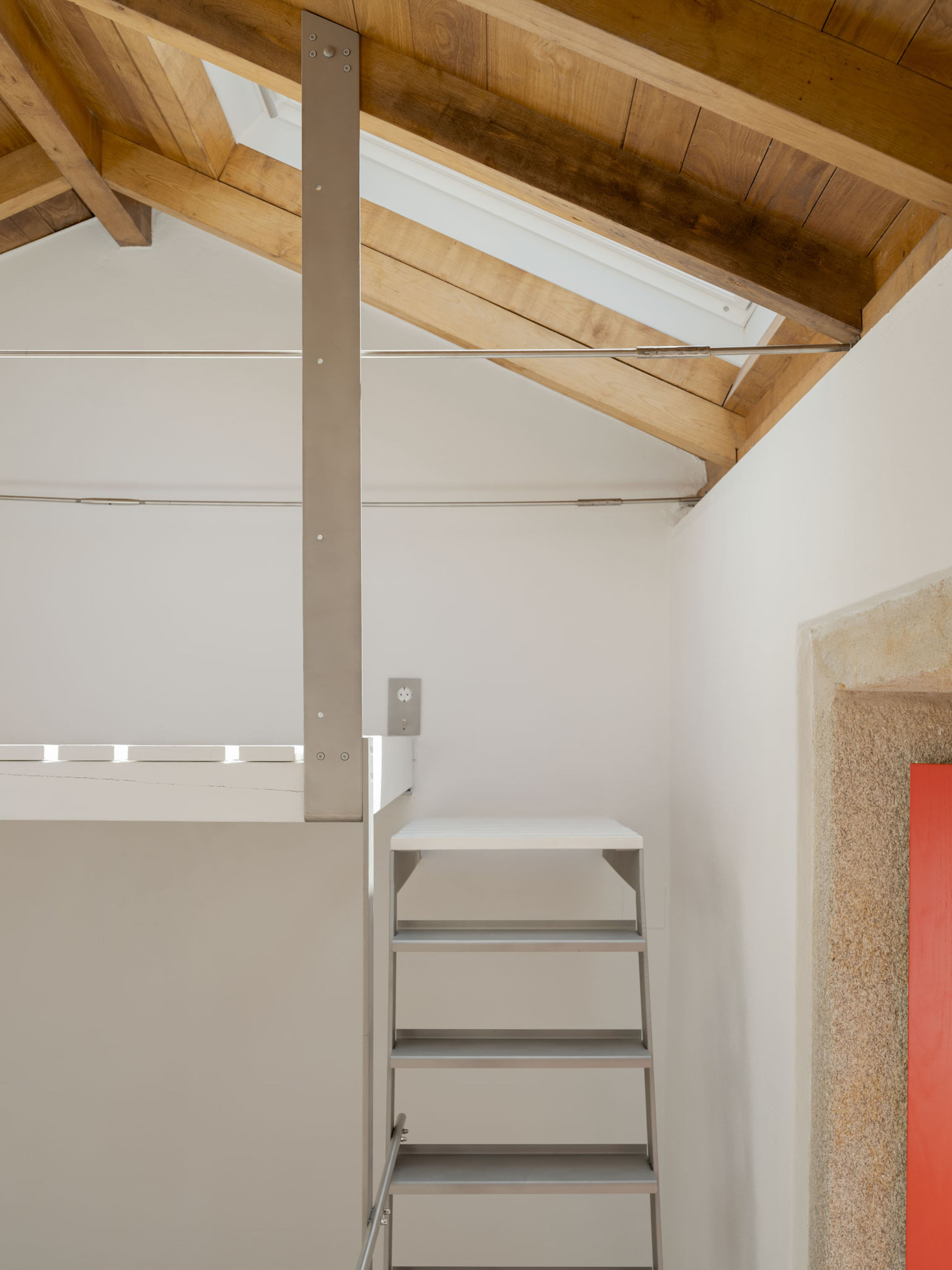 Pitched timber roof with a skylight, steel tie rods, a vertical steel strap and a metal ladder leading to a loft