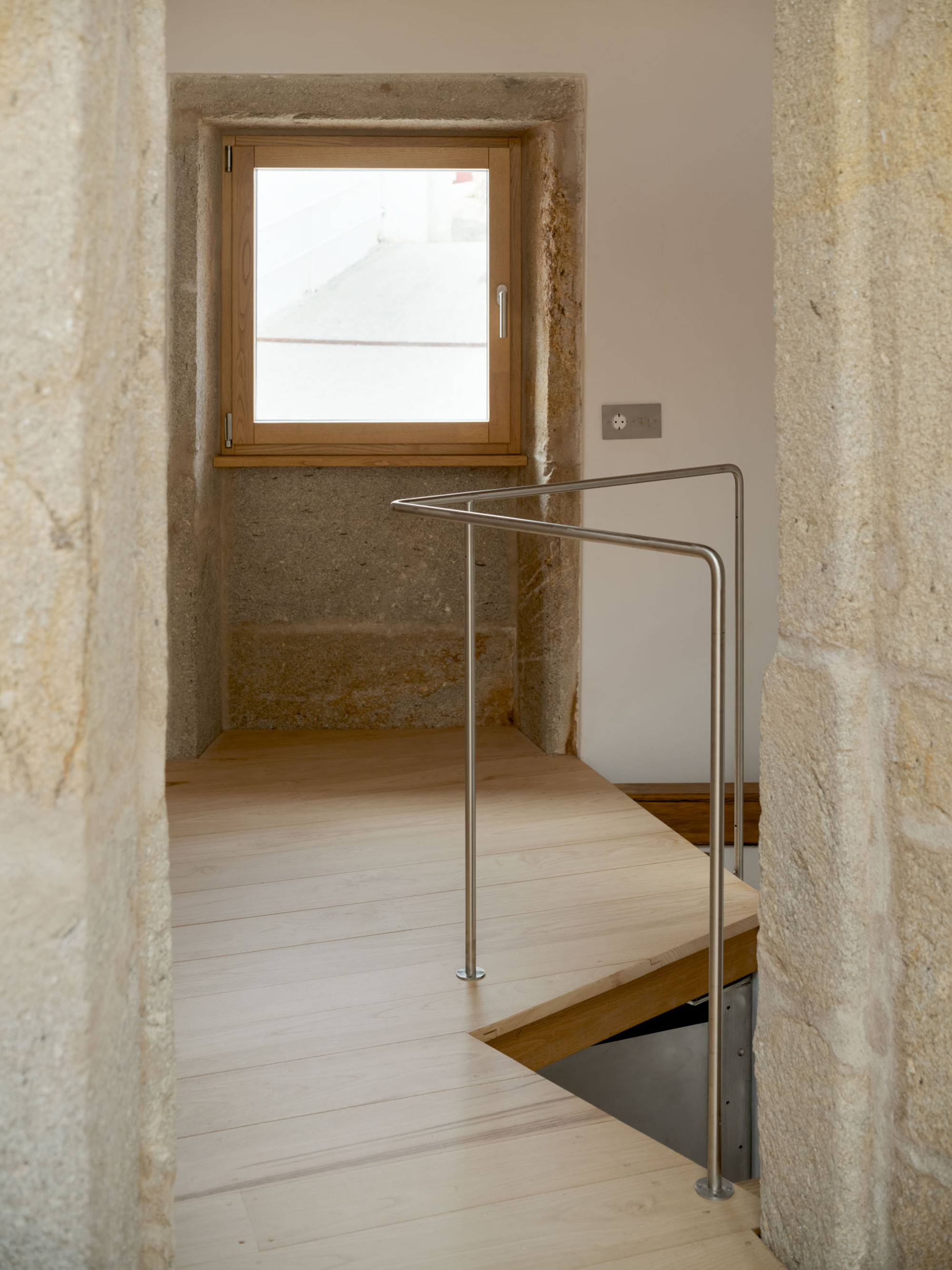 Stone-framed doorway opening onto a timber floor, a steel handrail and a deep-set window with oak frame