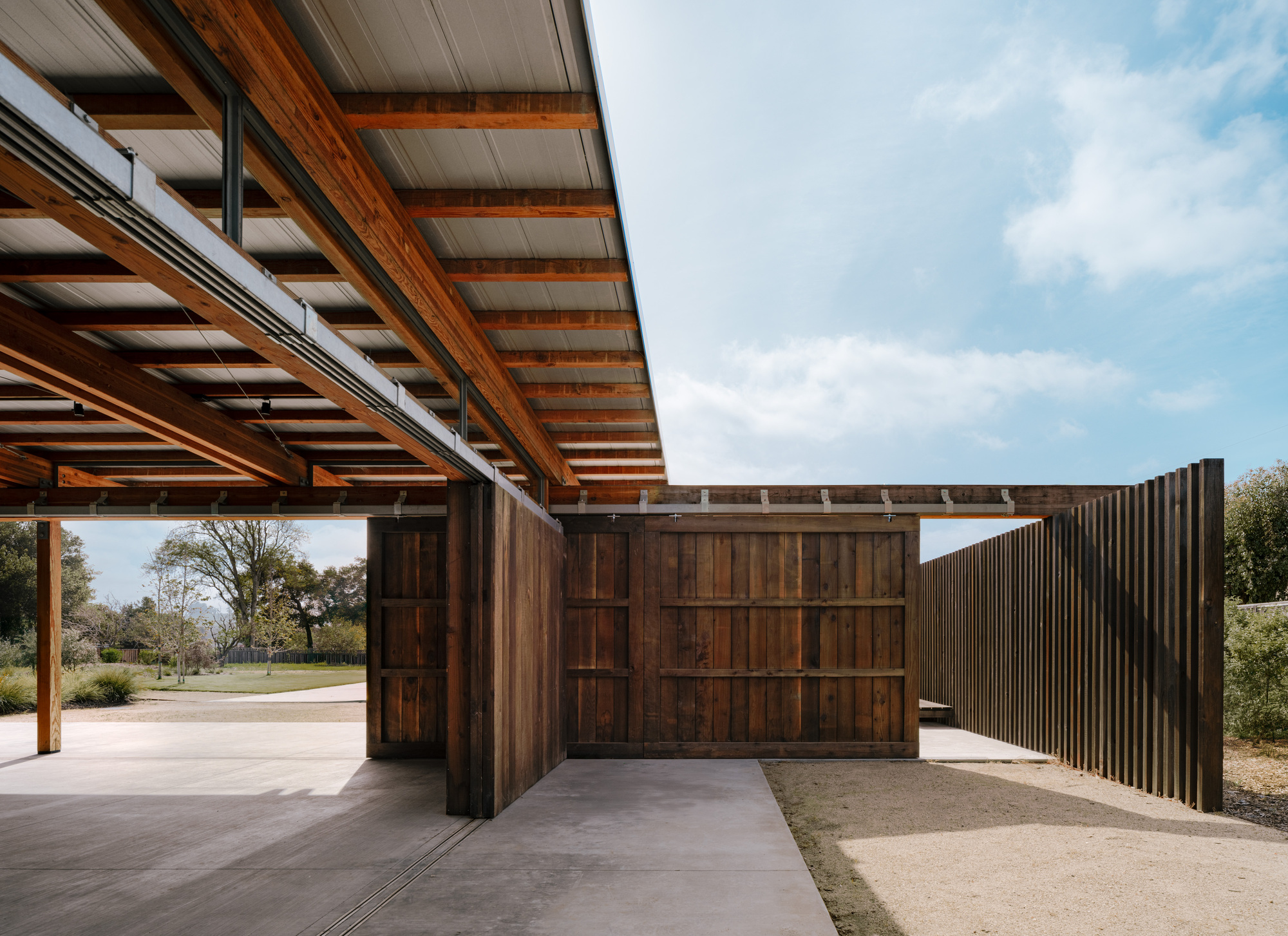 Underside of the timber roof beams above sliding wood panel doors and a slatted fence, in afternoon sun