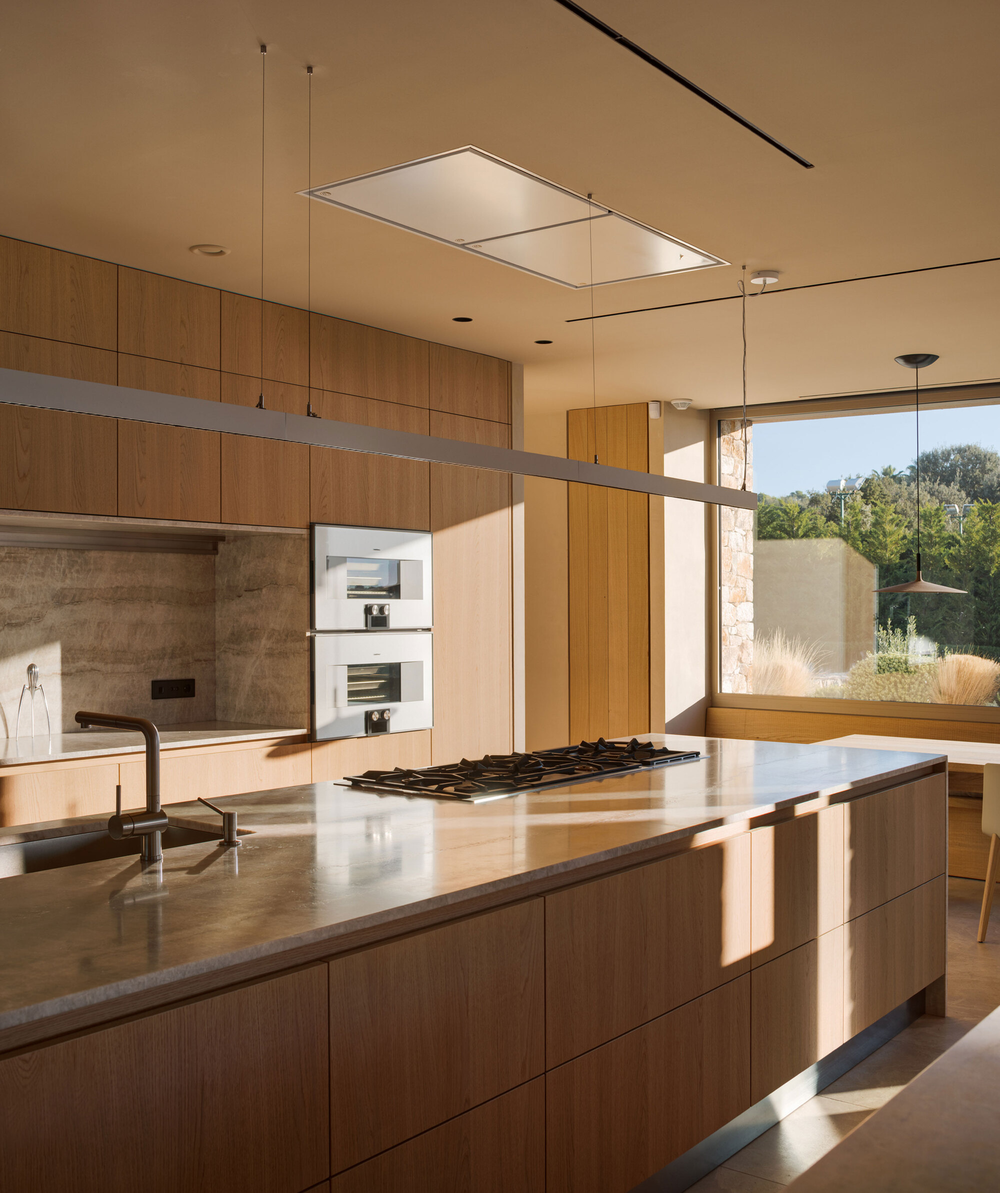 Kitchen island with a stone worktop and oak cabinetry, with low afternoon sun casting shadows across the front