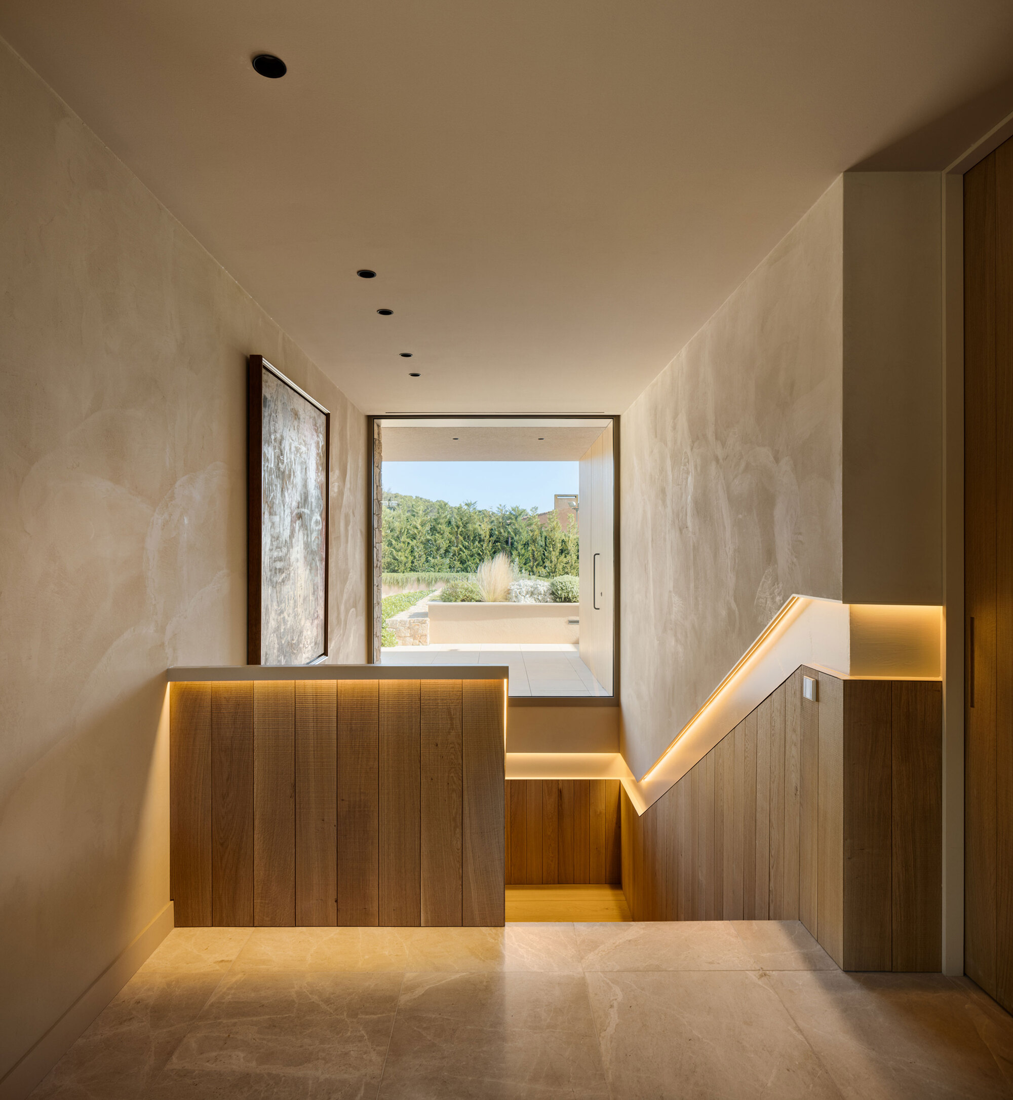 Stairwell with oak panelled balustrade and warm integrated handrail light, framed window looking onto a planted terrace