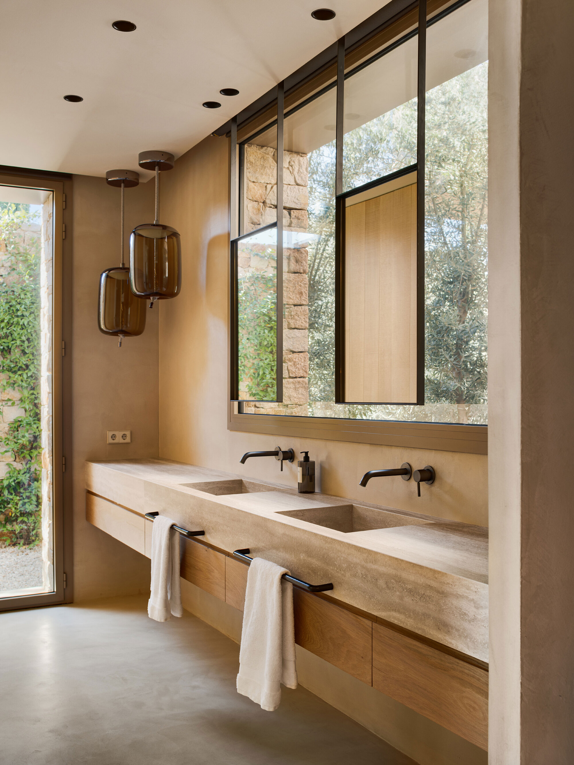 Bathroom with a double stone basin on an oak vanity, black taps and smoked glass pendants beside a window to greenery