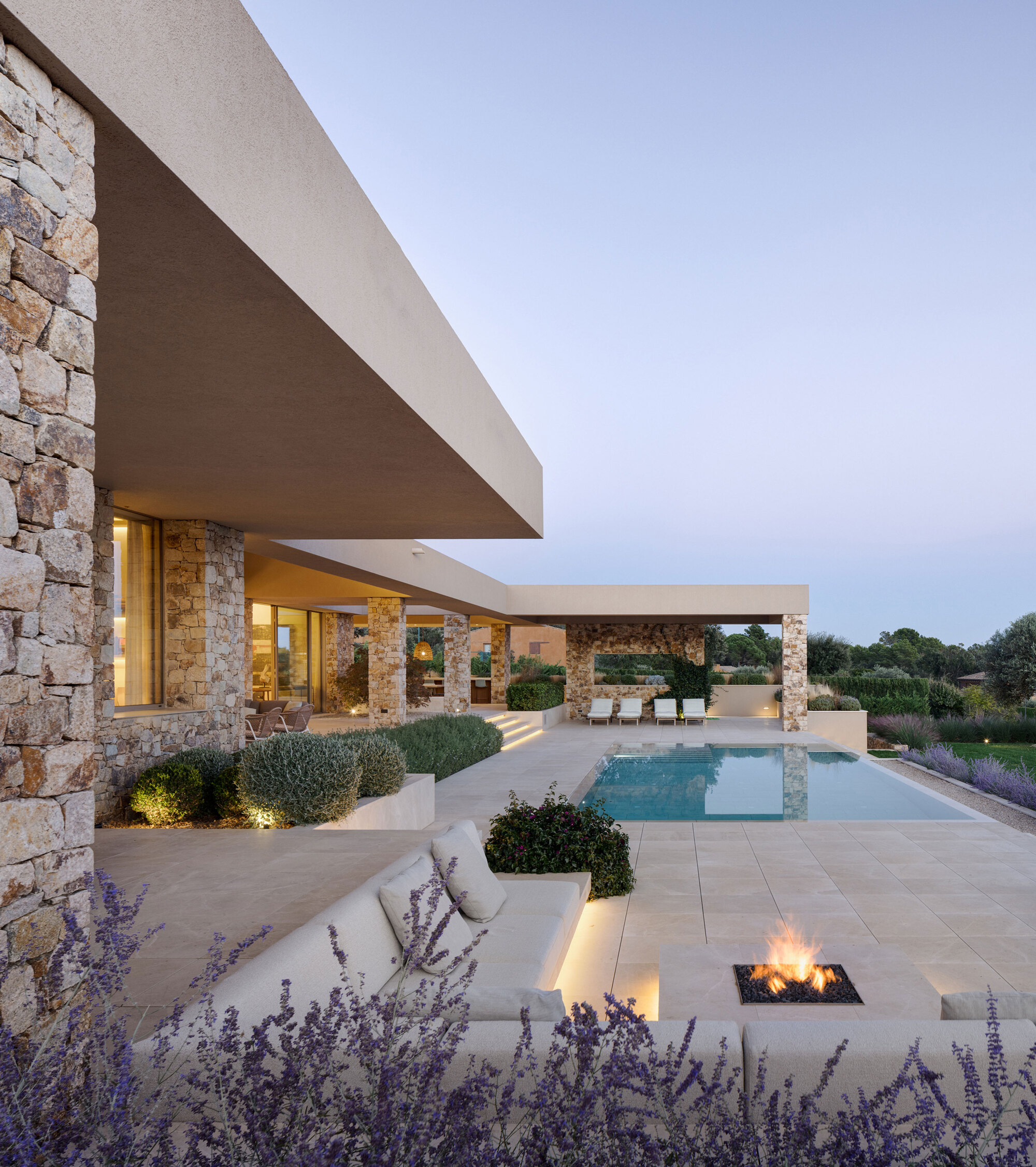 Terrace view along the stone piers to the pool, with a built-in sofa and lit fire pit among lavender