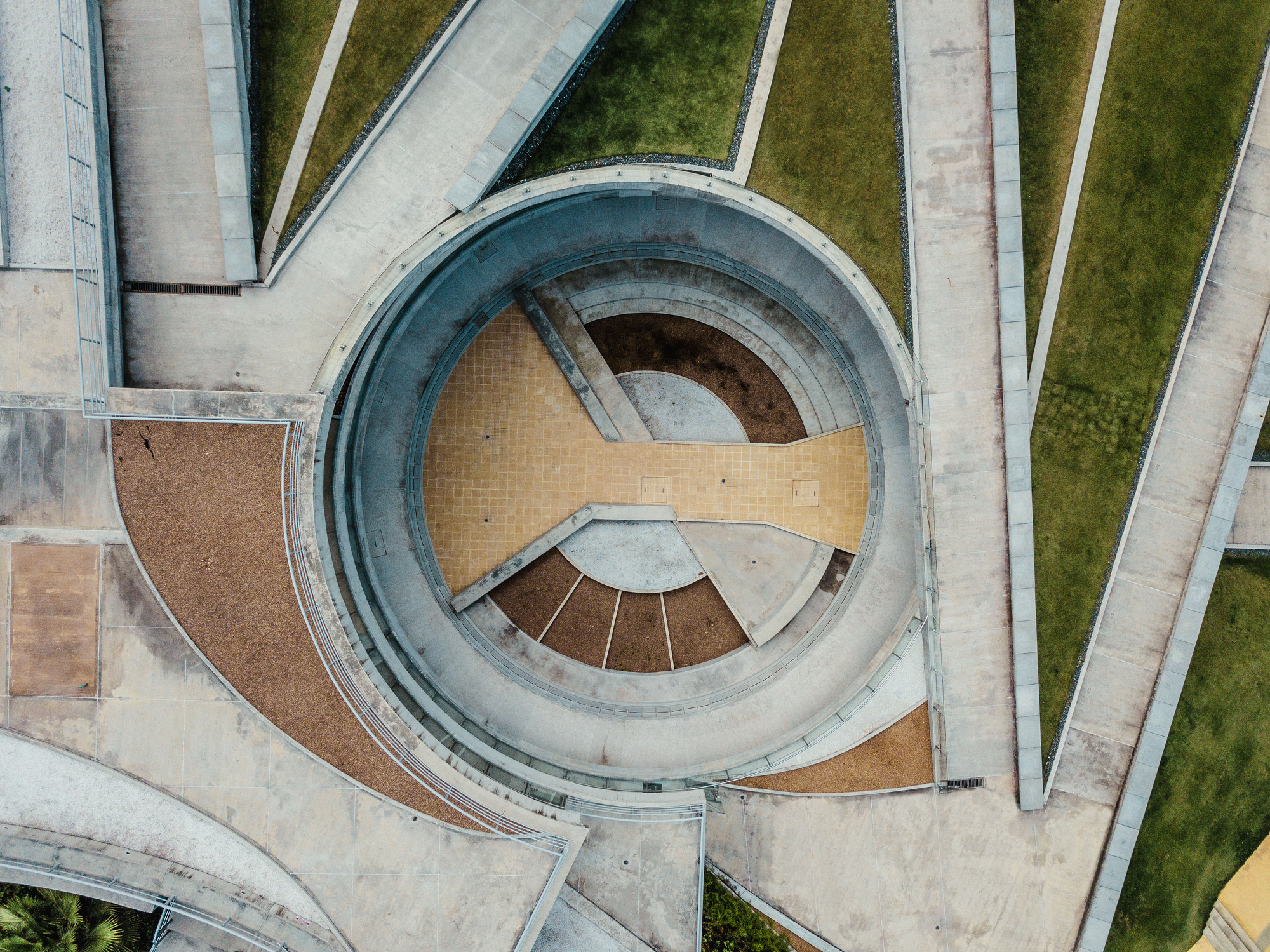 Top-down view of the circular amphitheater with yellow tile floor, tiered steps and radiating concrete paths beside grass strips