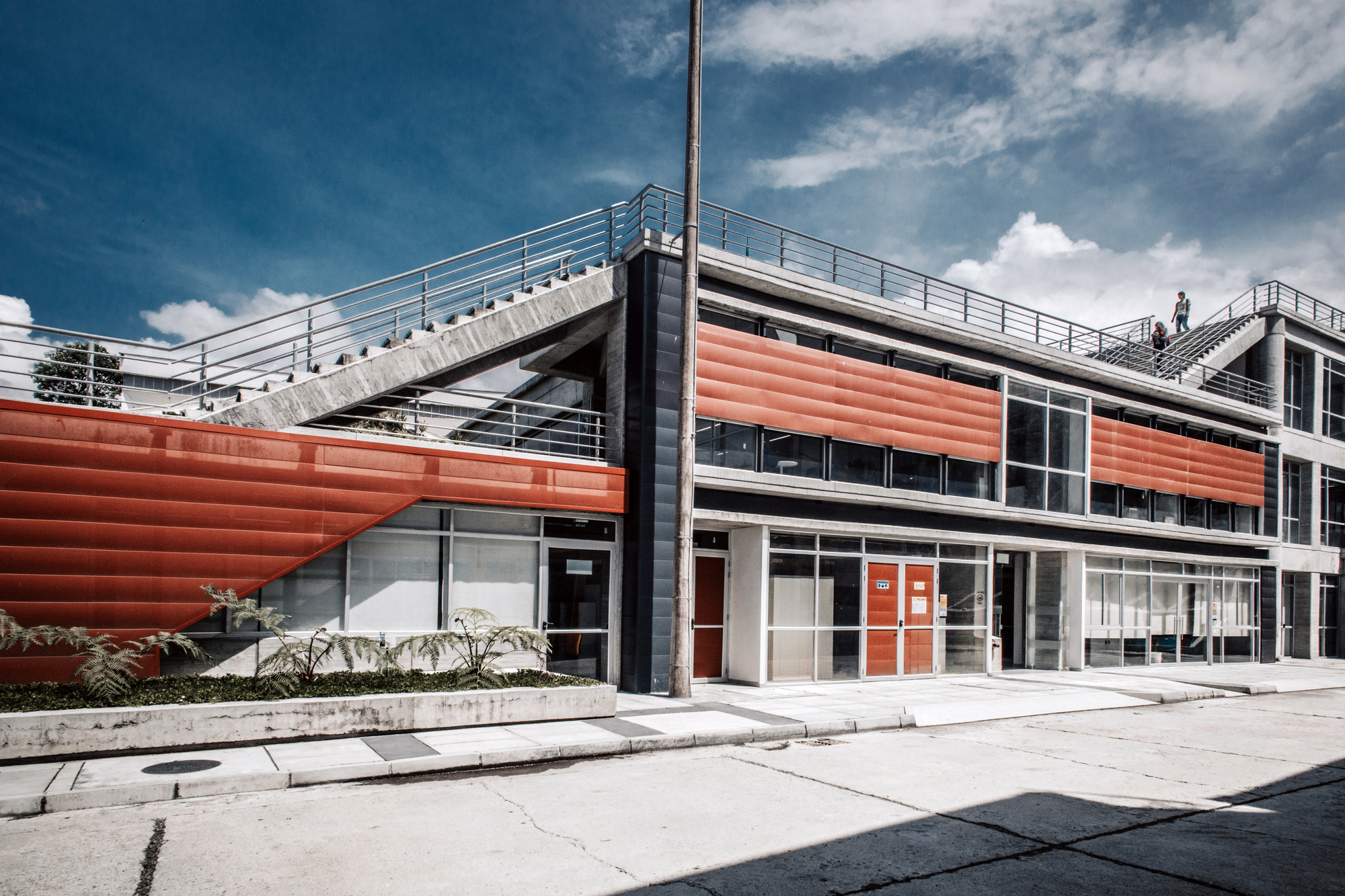 Two-storey facade with corrugated orange metal panels and a concrete exterior stair, under a deep blue sky with scattered clouds