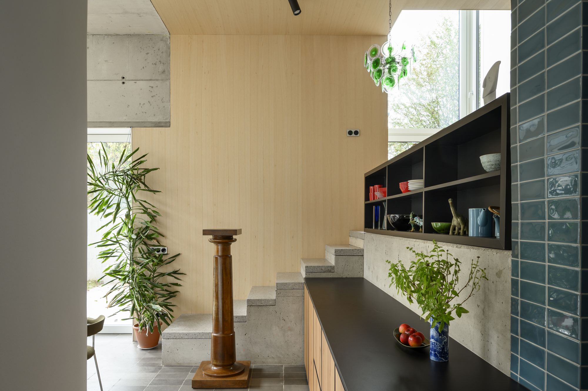 Concrete stair beside a black kitchen counter and blue glazed tile wall, with a tall potted plant in daylight