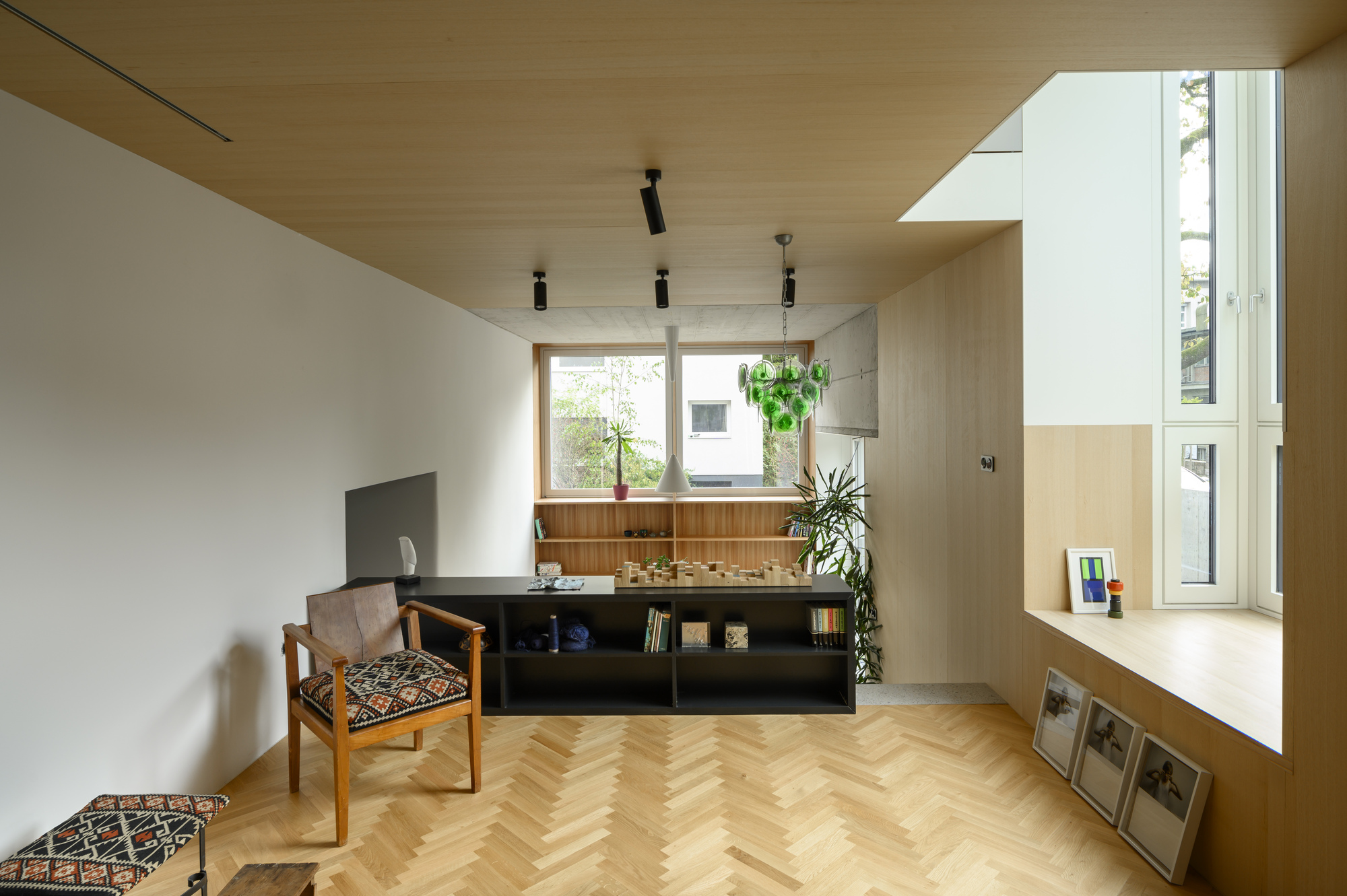 Living room with herringbone floor, timber ceiling and a window seat in a tall side window, with a low black shelf unit