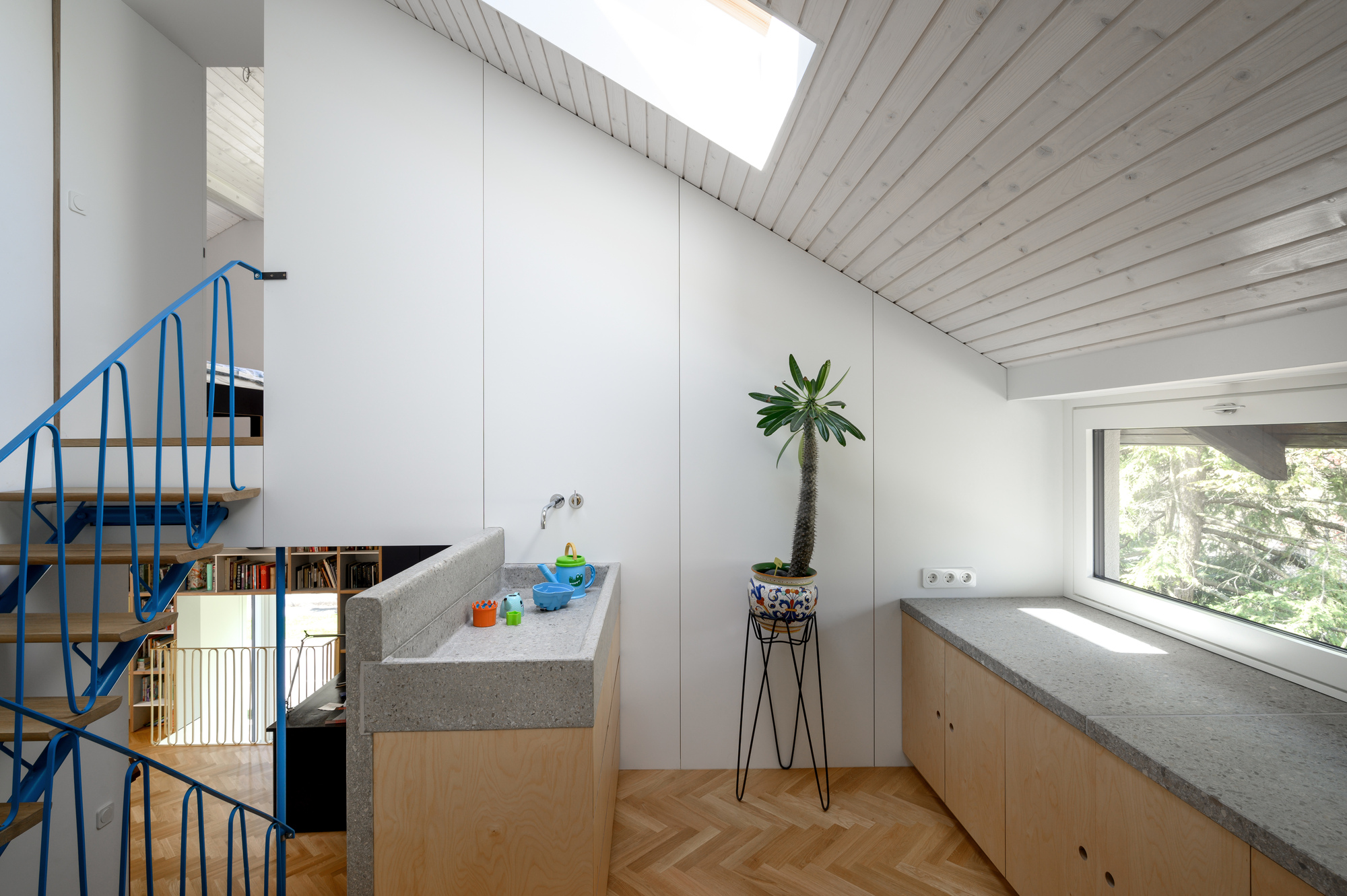 Attic room with terrazzo-topped sink and counter, sloping timber ceiling, skylight and potted plant beside a blue stair railing