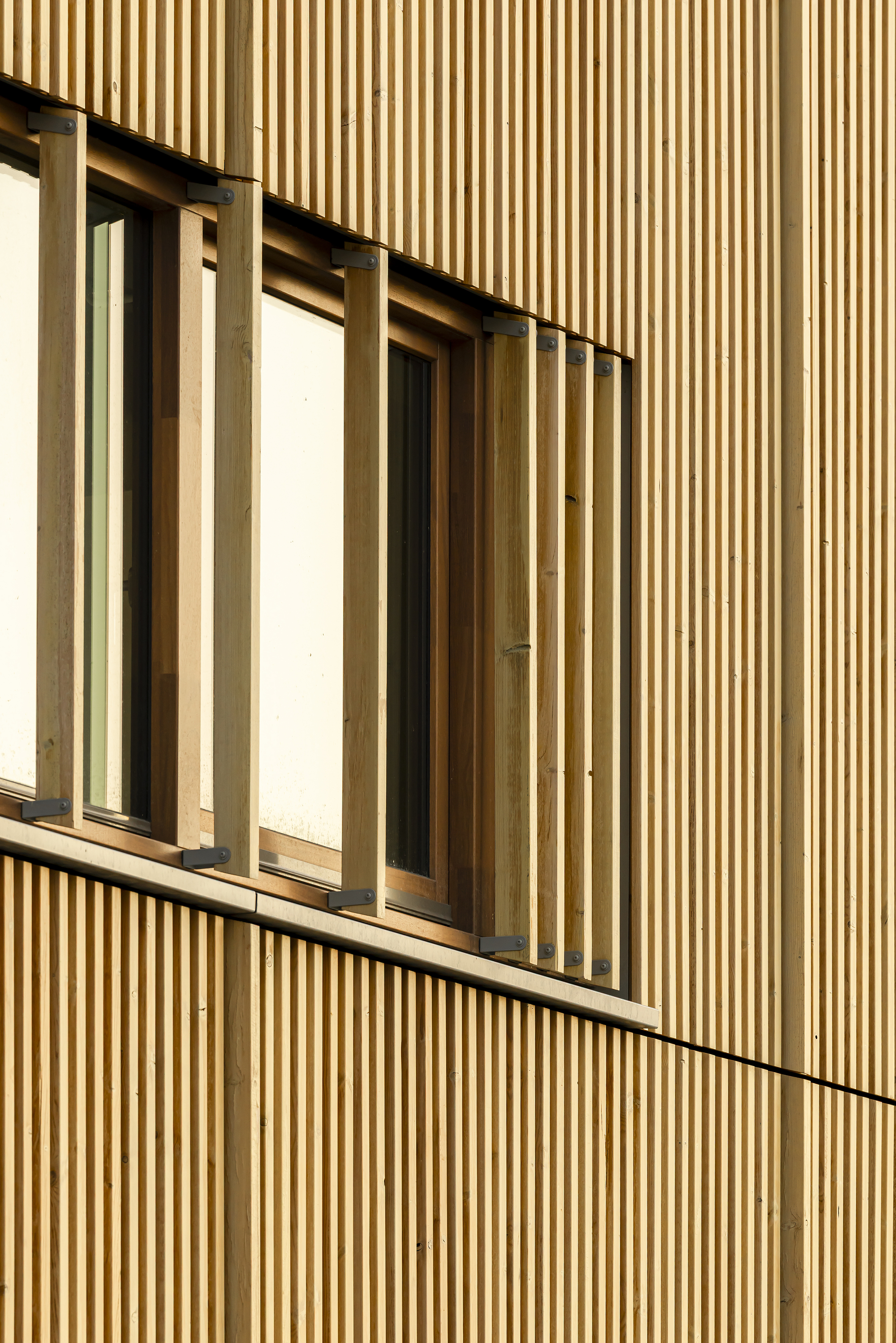 Close-up of vertical timber battens and operable wooden shutters beside a window, lit by low warm sun