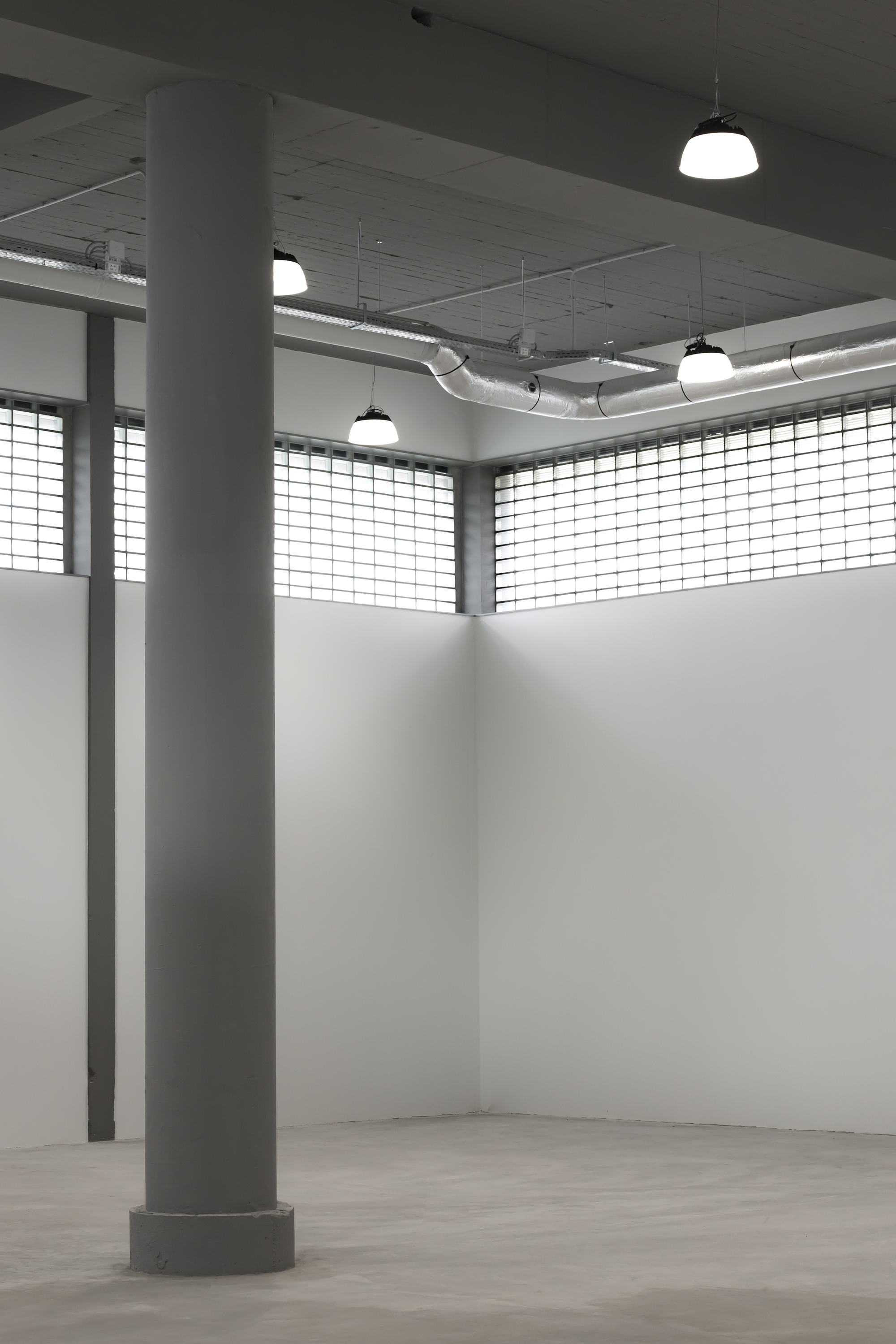 Empty room with a round concrete column, glass block clerestory windows and hanging pendant lamps over exposed ductwork