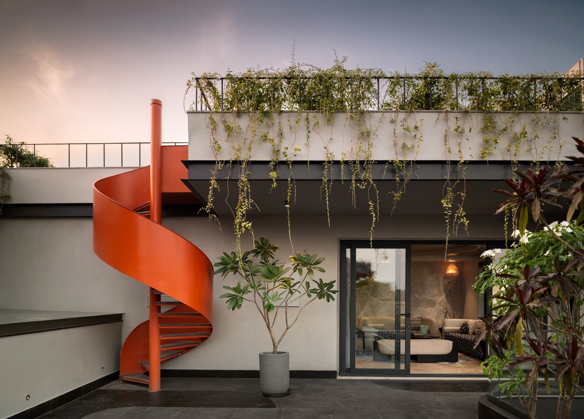 Orange spiral steel staircase beside a terrace where vines hang from the upper planter at dusk