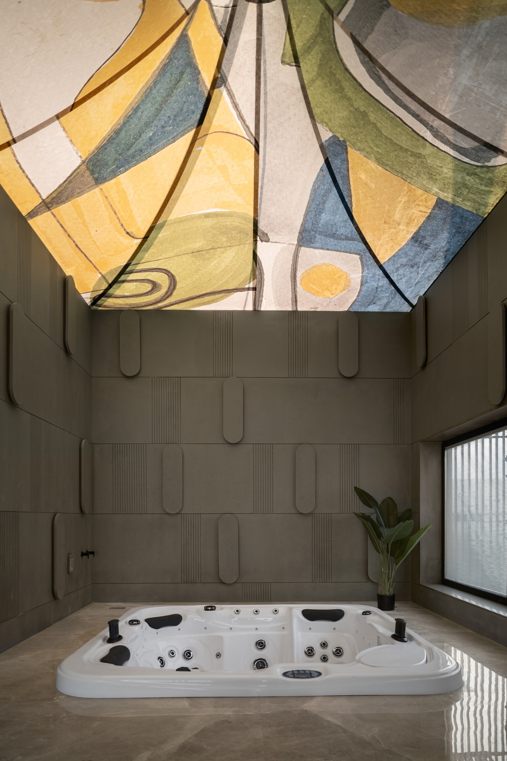 Sunken spa tub in a stone-clad room beneath a painted abstract ceiling in yellow, blue and green