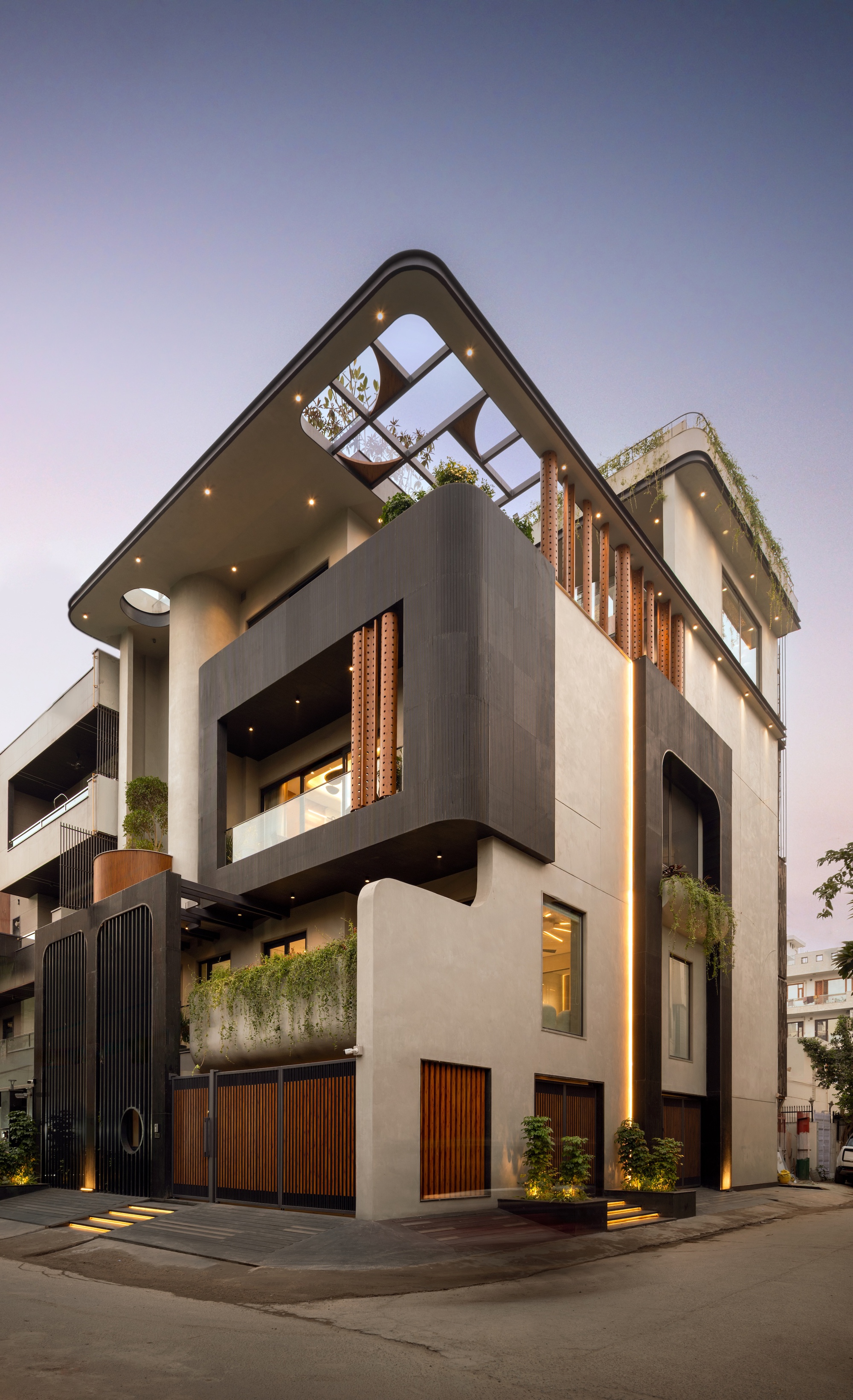 Corner view of the stacked house at dusk with warm recessed lights, a dark framed balcony and vertical light strip